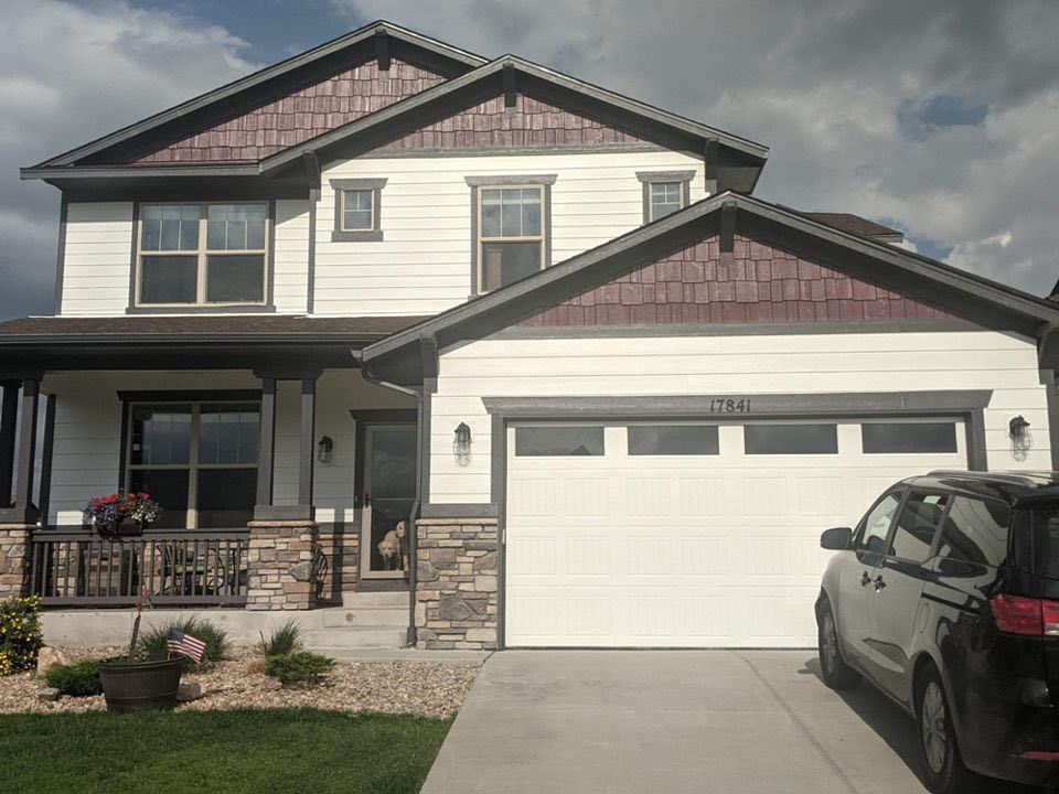 A two-story house with white siding, dark brown trim, stone accents, a front porch, and a white two-car garage.