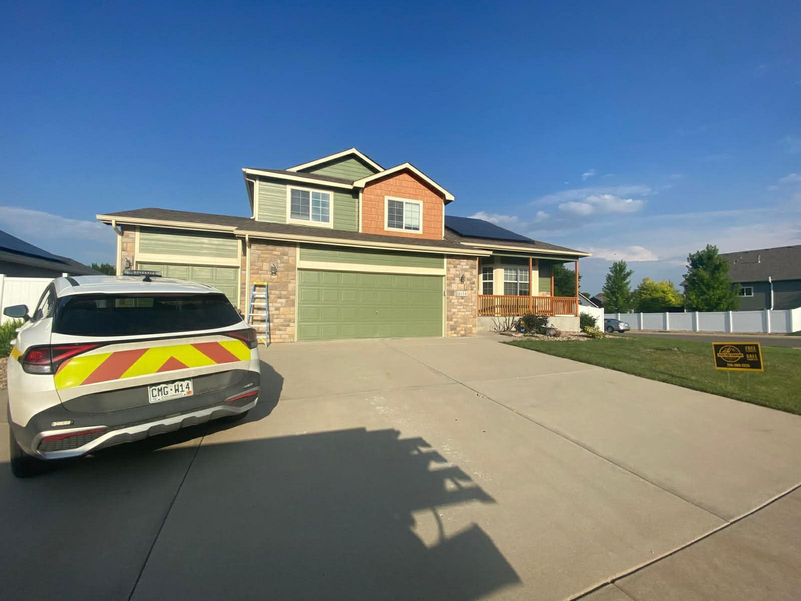 A white SUV with yellow and orange warning chevrons parked in the driveway of a two-story home with a green garage door.