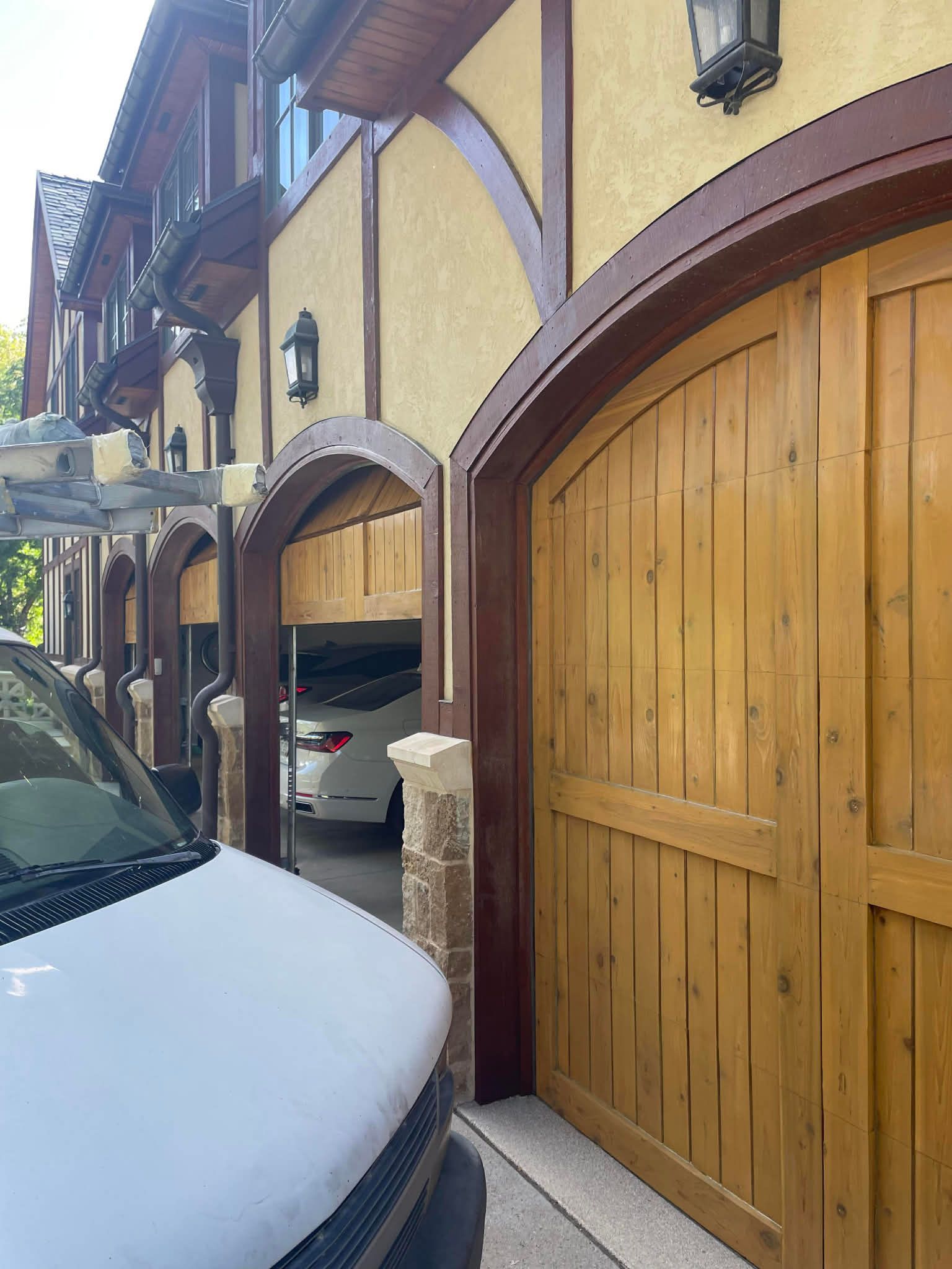 A view of a yellow Tudor-style building with arched wooden garage doors, partly obscured by the hood of a white vehicle.