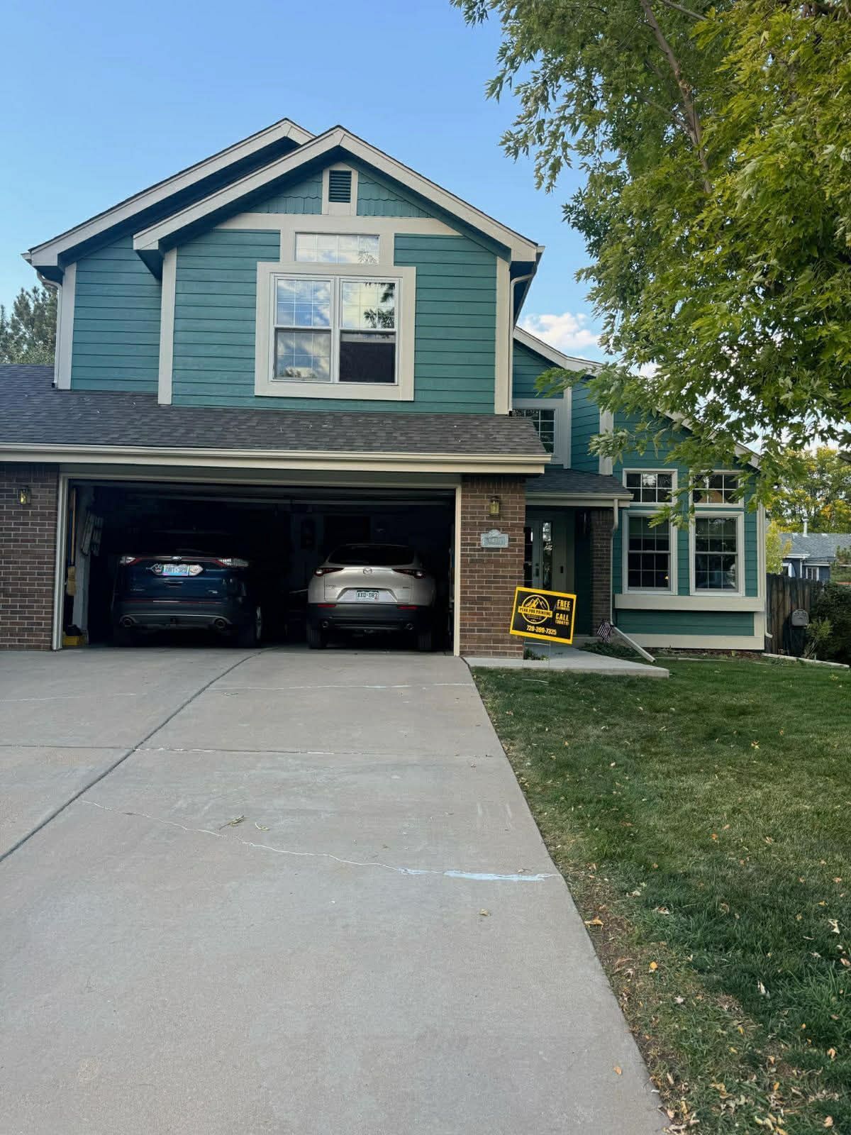A teal, two-story suburban home with a two-car garage, a concrete driveway, and a tree in the front yard.