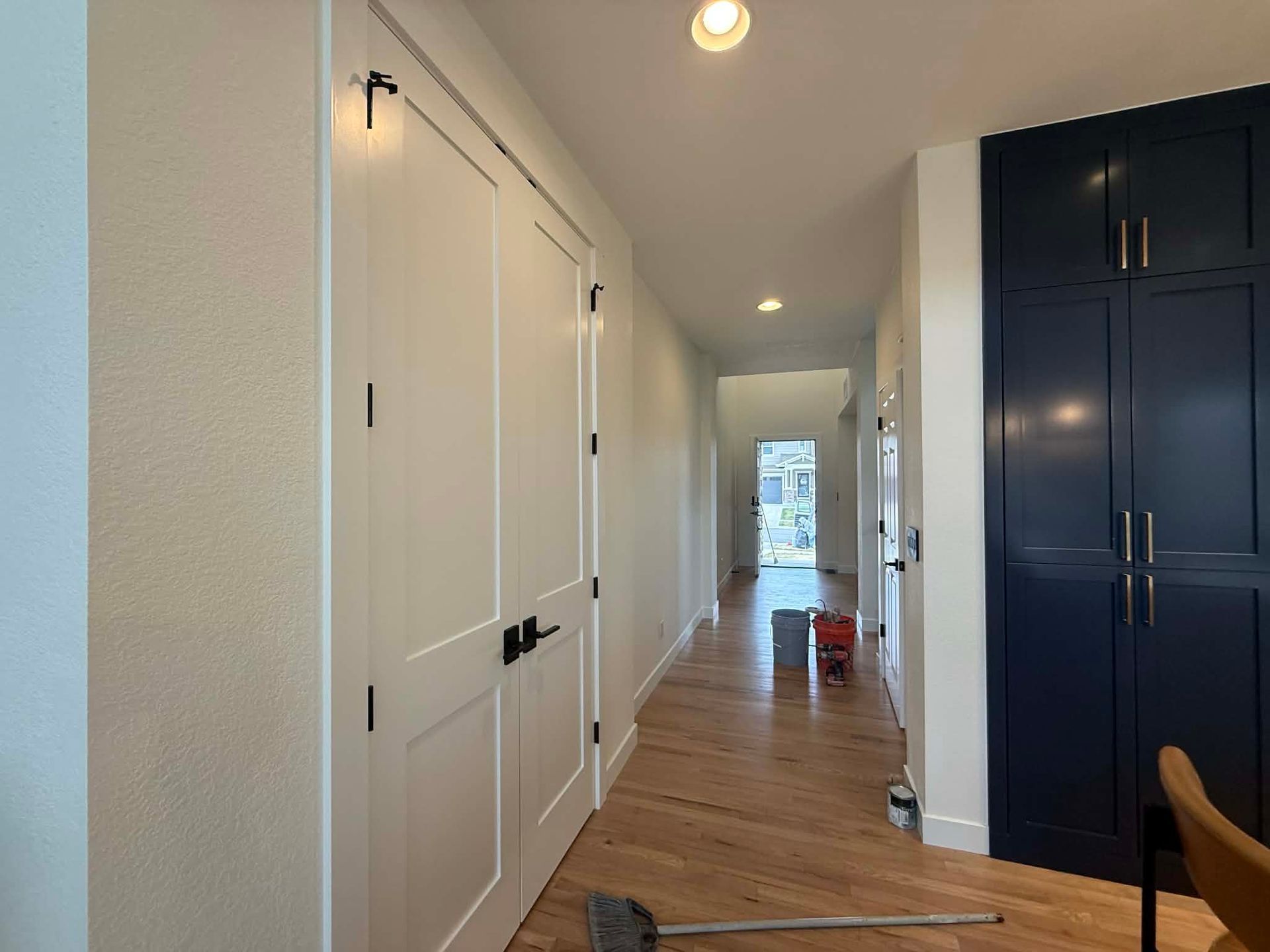 A hallway with light wood floors, white double doors on the left, and a dark blue floor-to-ceiling cabinet on the right.