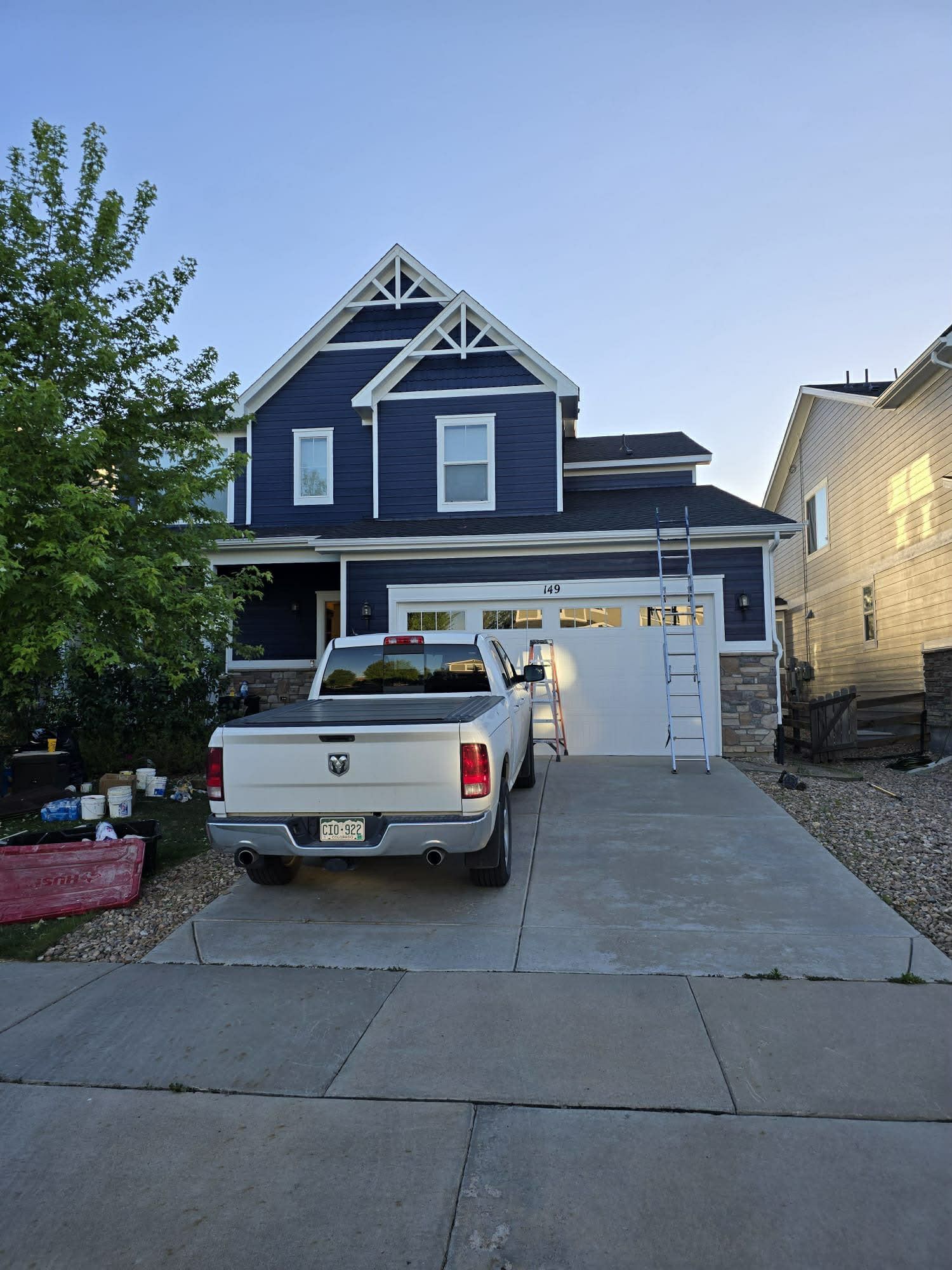 A dark blue two-story house with a stone base and white garage door, featuring a white pickup truck parked in the driveway.