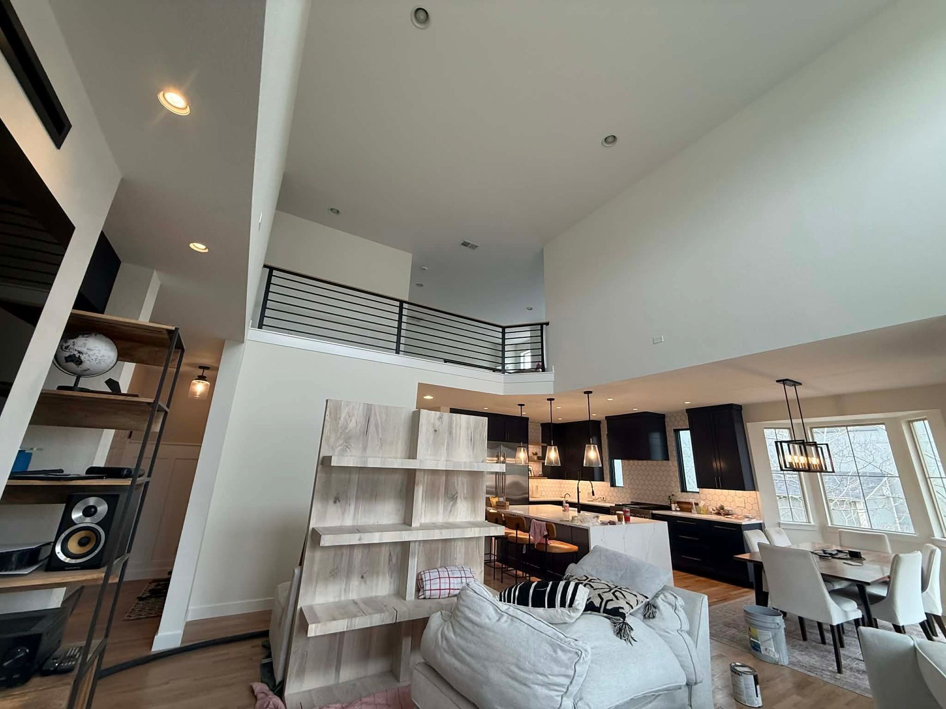 A bright, open-plan living room with high ceilings, a balcony overlooking the area, and a kitchen in the background.
