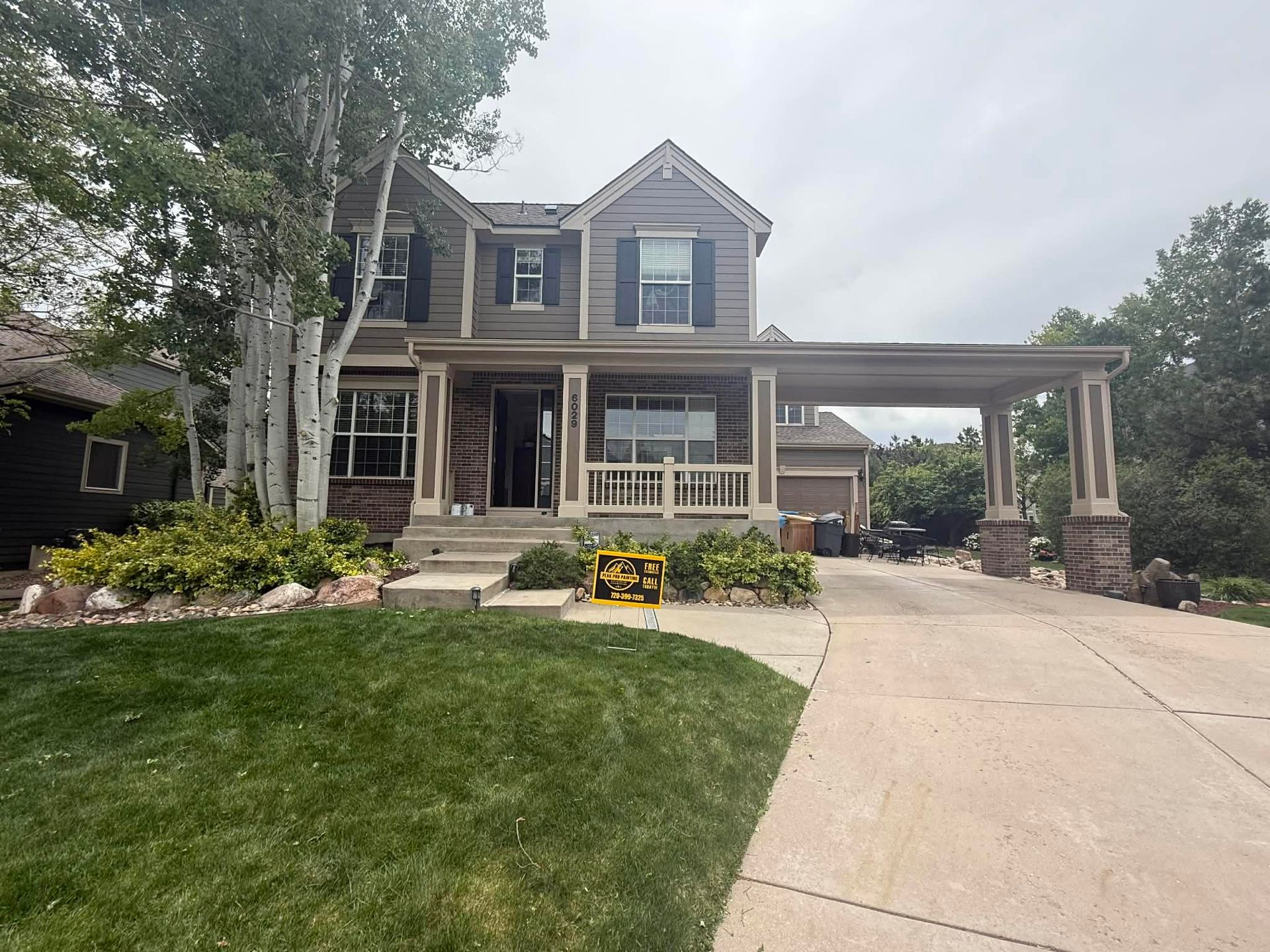 A two-story grey house with a front porch, an attached carport on the right, and a grassy front lawn.