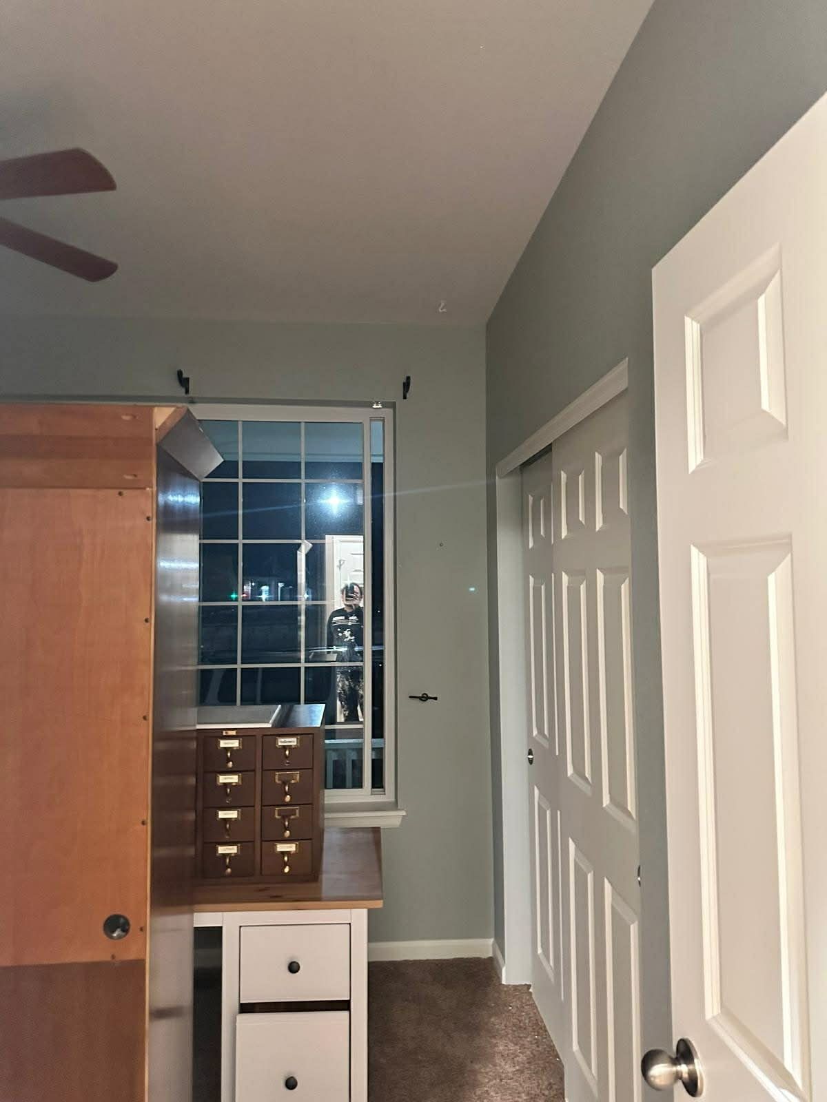 A view of a bedroom interior featuring a desk, a small filing cabinet, a window at night, and a white sliding closet door.