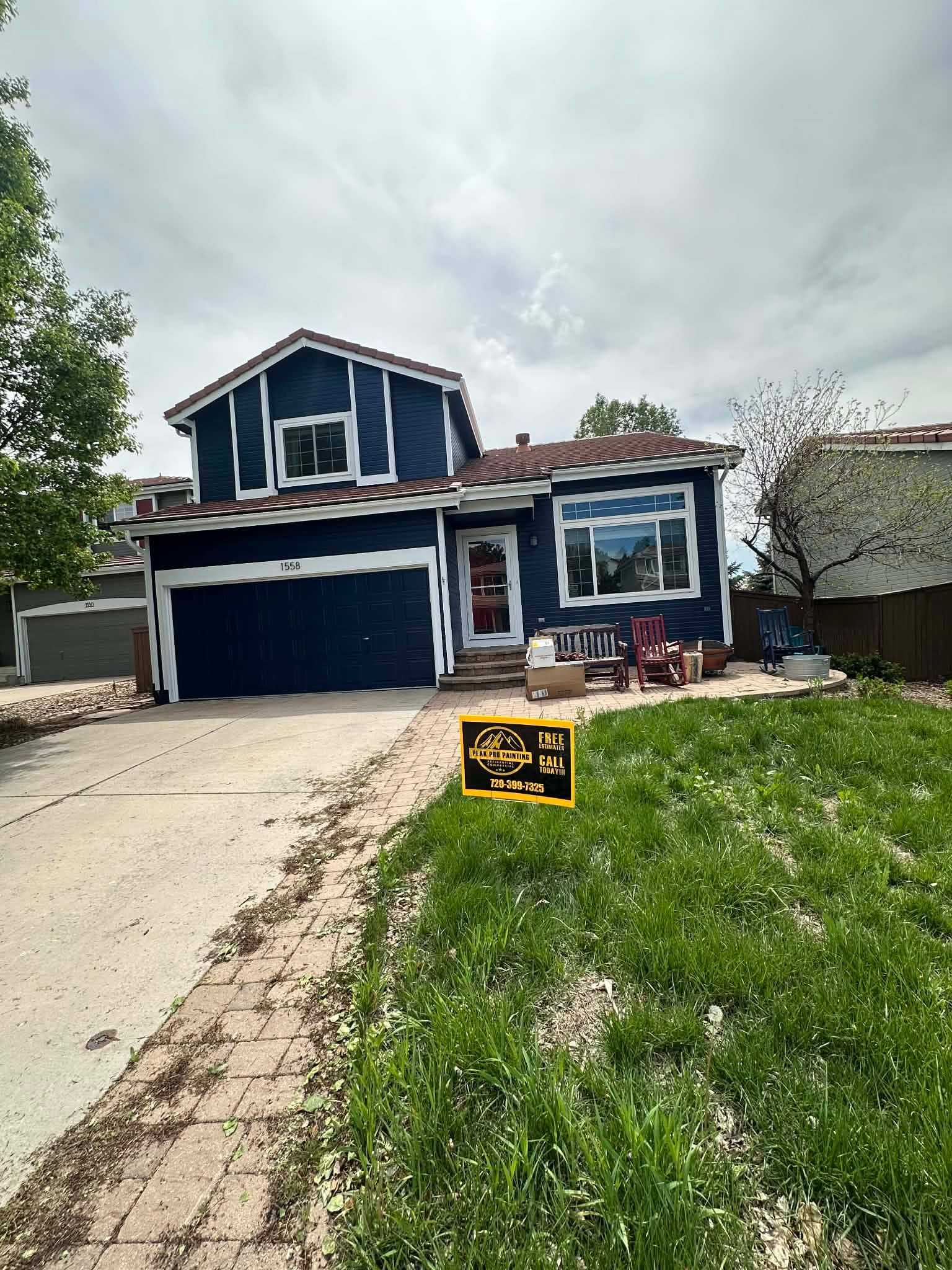 A two-story house under renovation with dark blue siding and white trim, featuring a driveway and a grassy front yard.