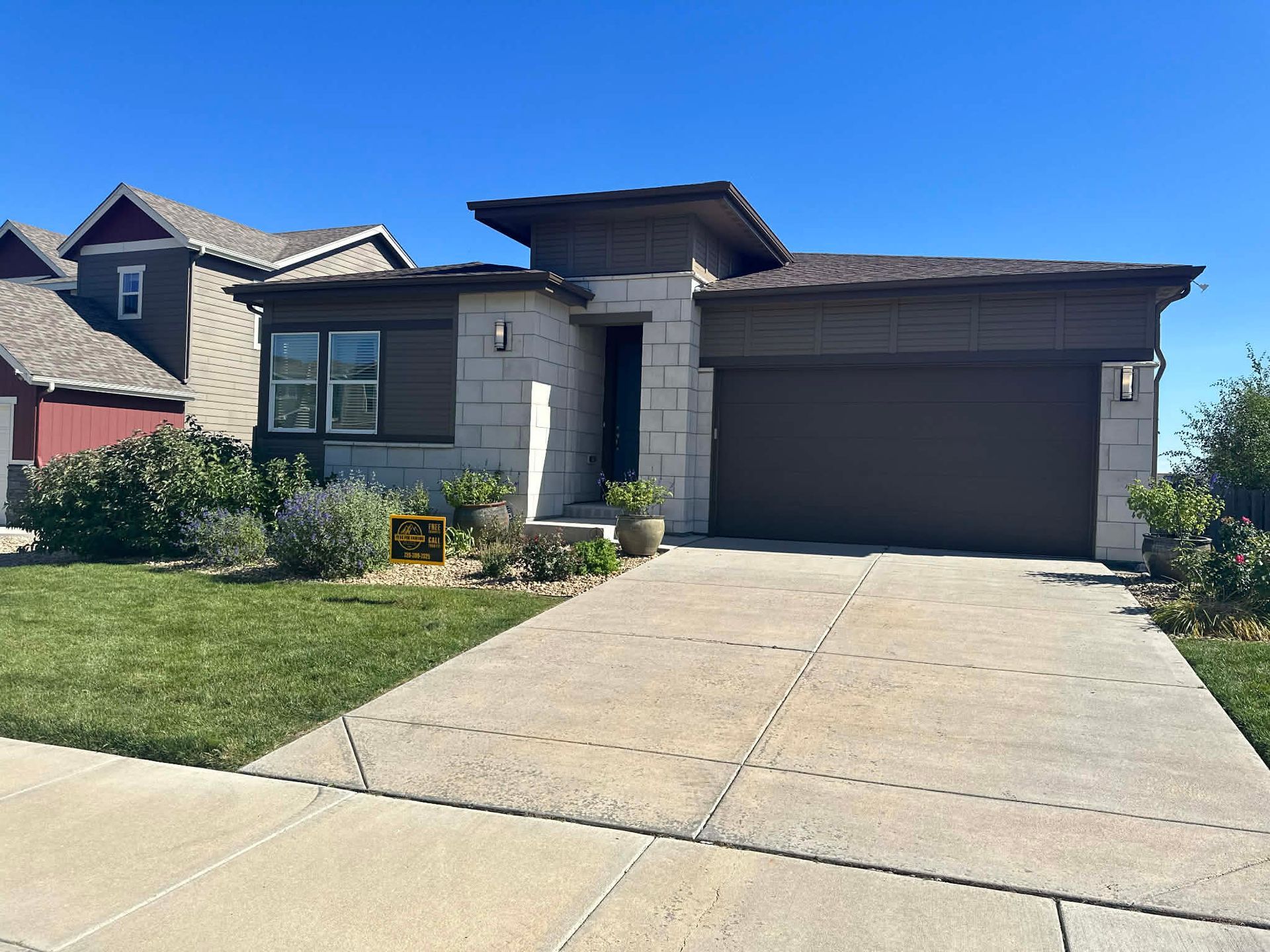 A single-story suburban house with stone and brown siding, a two-car garage, a concrete driveway, and a manicured lawn.