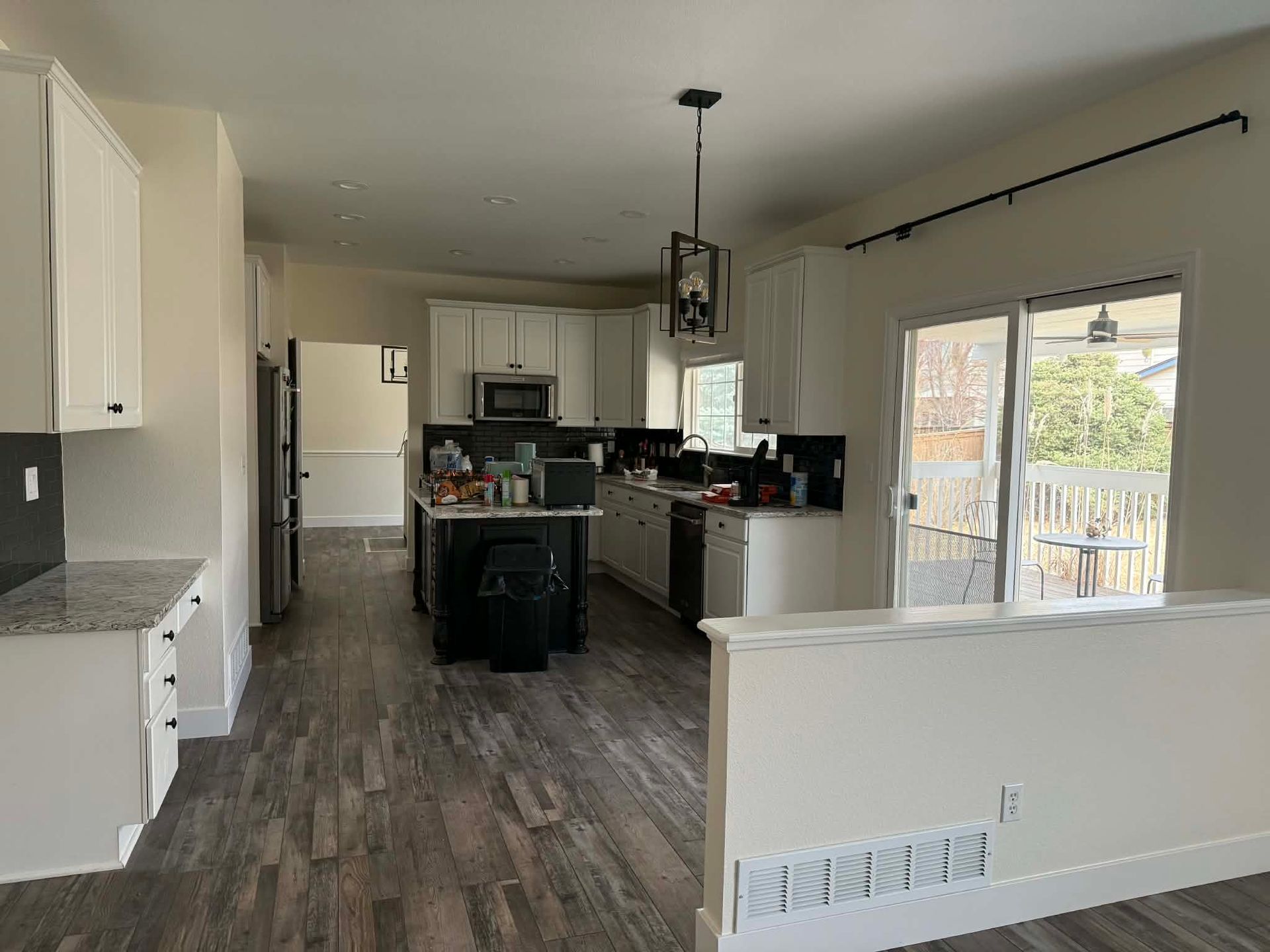 A modern kitchen with white cabinets, dark countertops, wood-look flooring, and a sliding glass door to a deck.