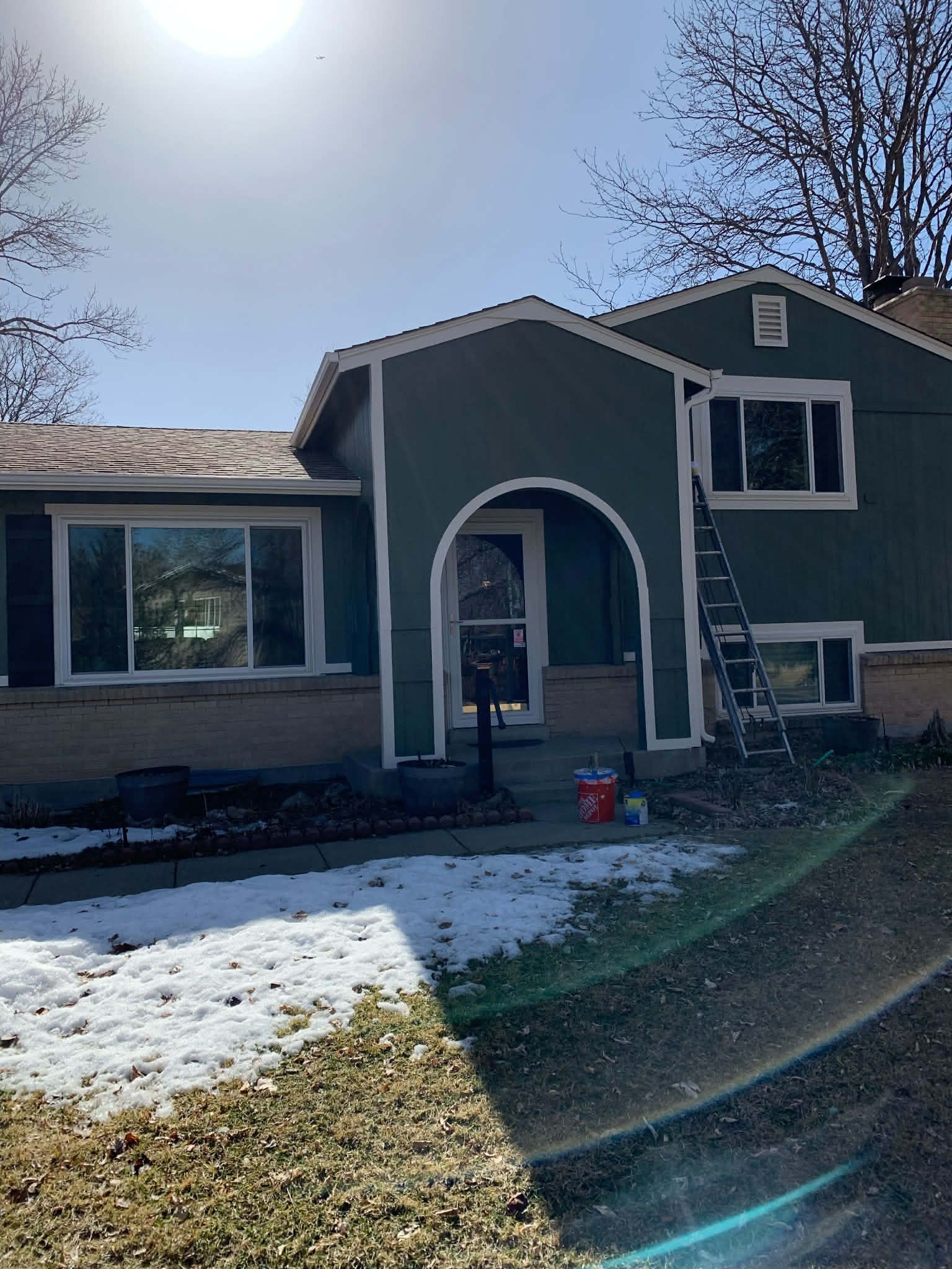 A two-story house with a dark green exterior, a front archway, and a ladder leaning against the side.