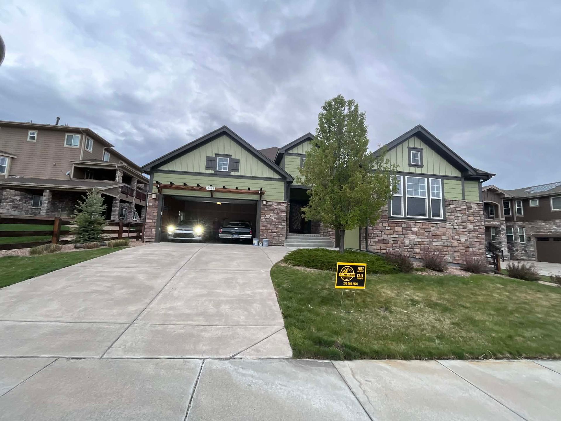 A two-story suburban home with stone and green siding, a large driveway, and a yellow sign on the front lawn.