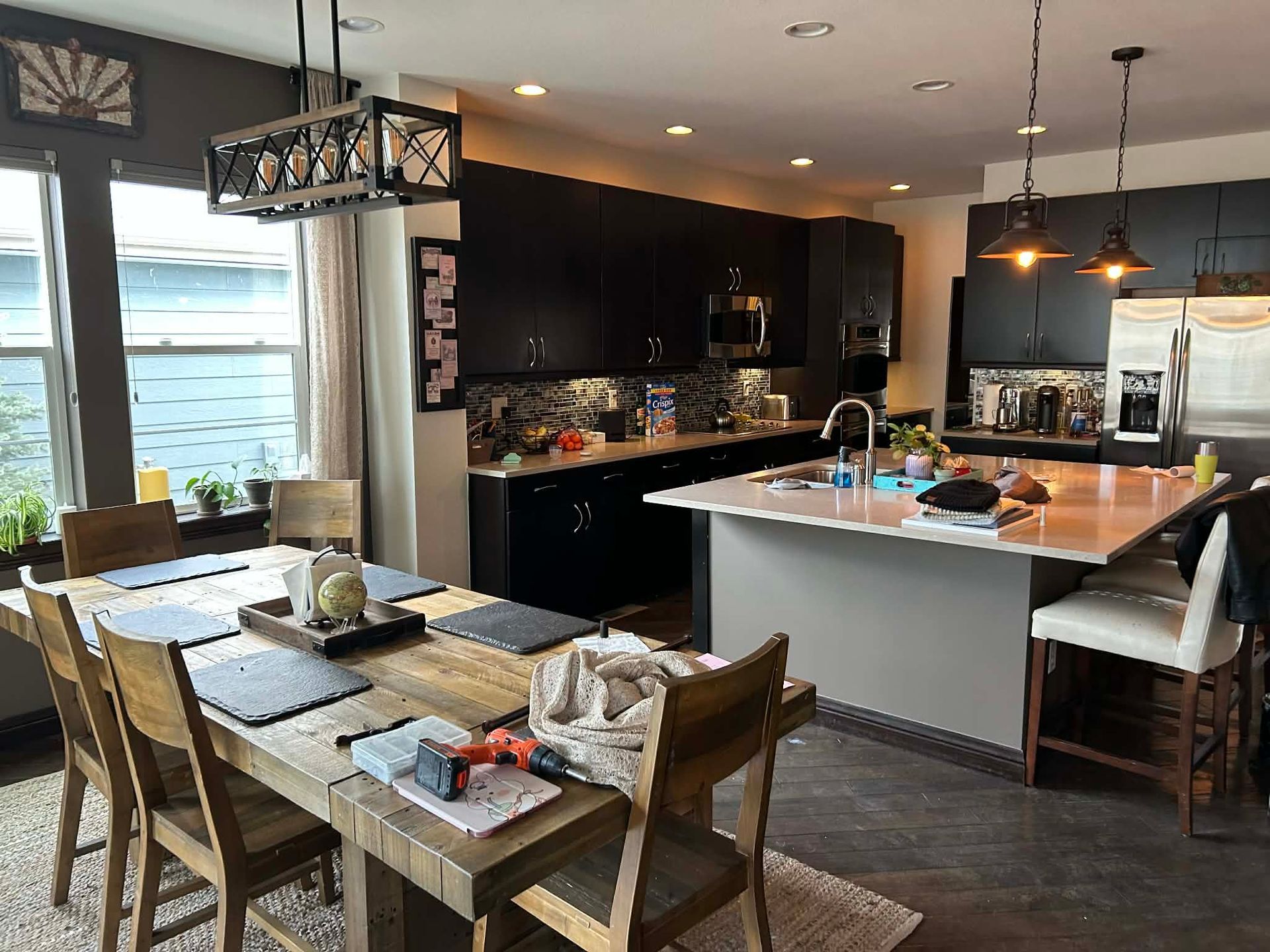 A modern dining room adjacent to an open-plan kitchen with a large island, dark cabinets, and pendant lighting.