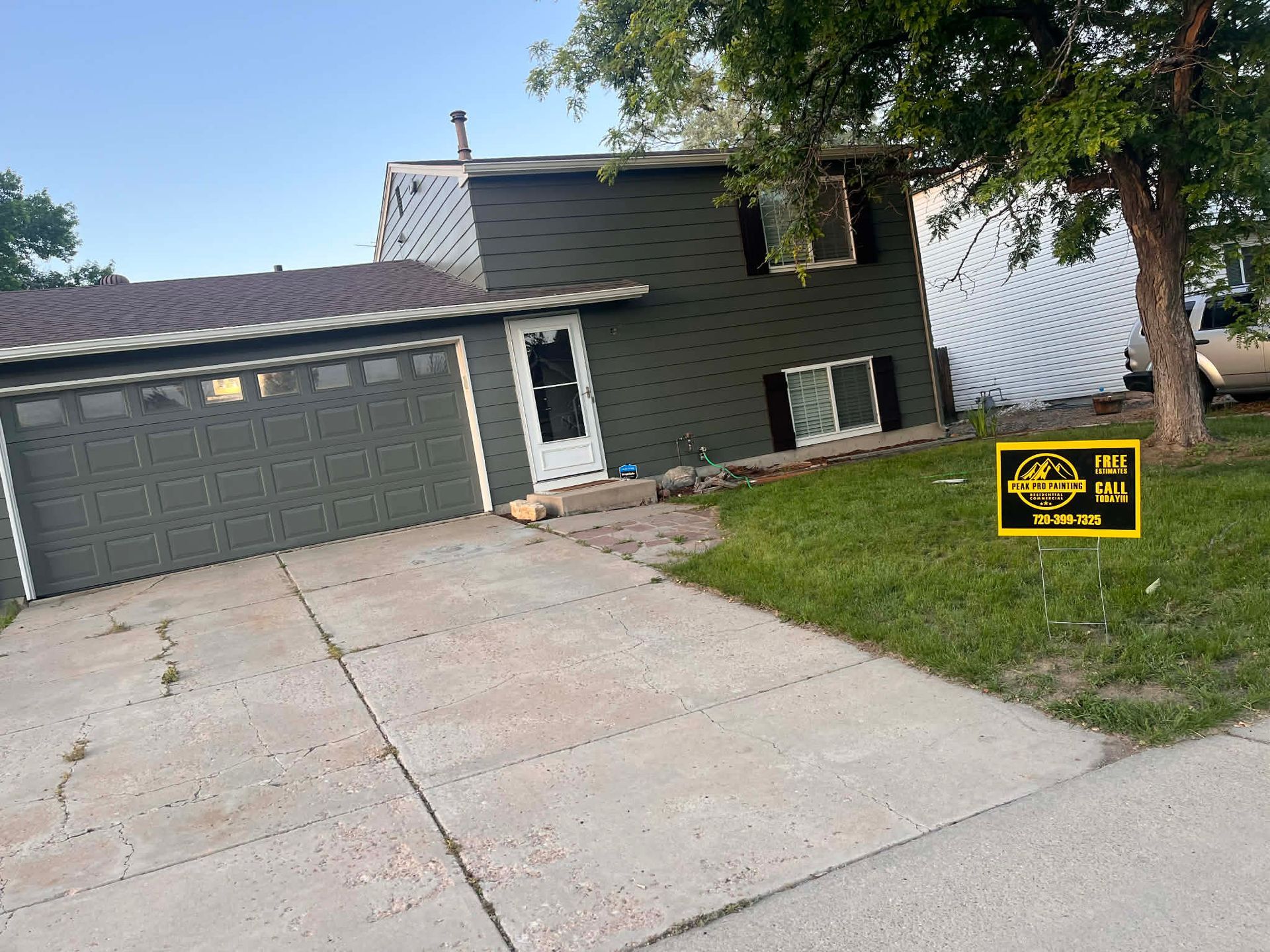 A dark green split-level house with a gray garage door, a white front door, and a yellow sign on the front lawn.