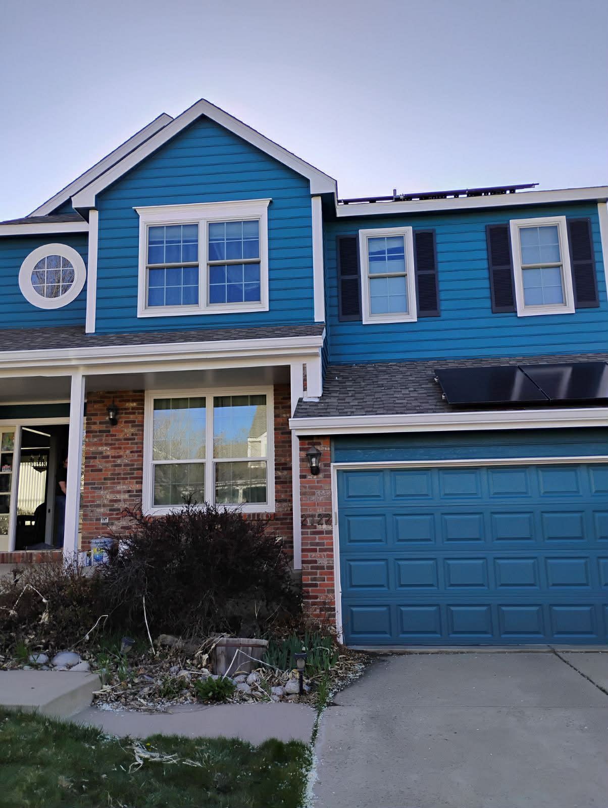 A two-story house with blue siding and brick accents, a matching blue garage door, and a circular window on the left.
