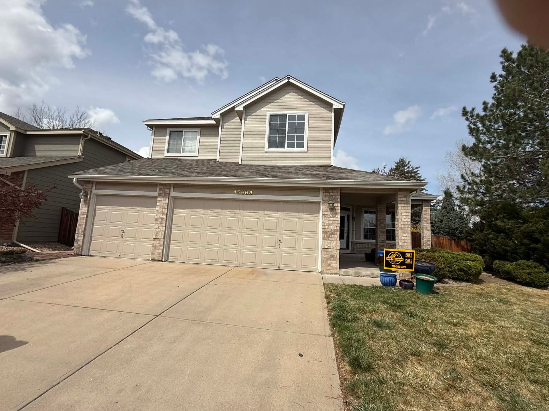 A two-story suburban home with a three-car garage, light-colored siding, stone accents, and a front driveway.