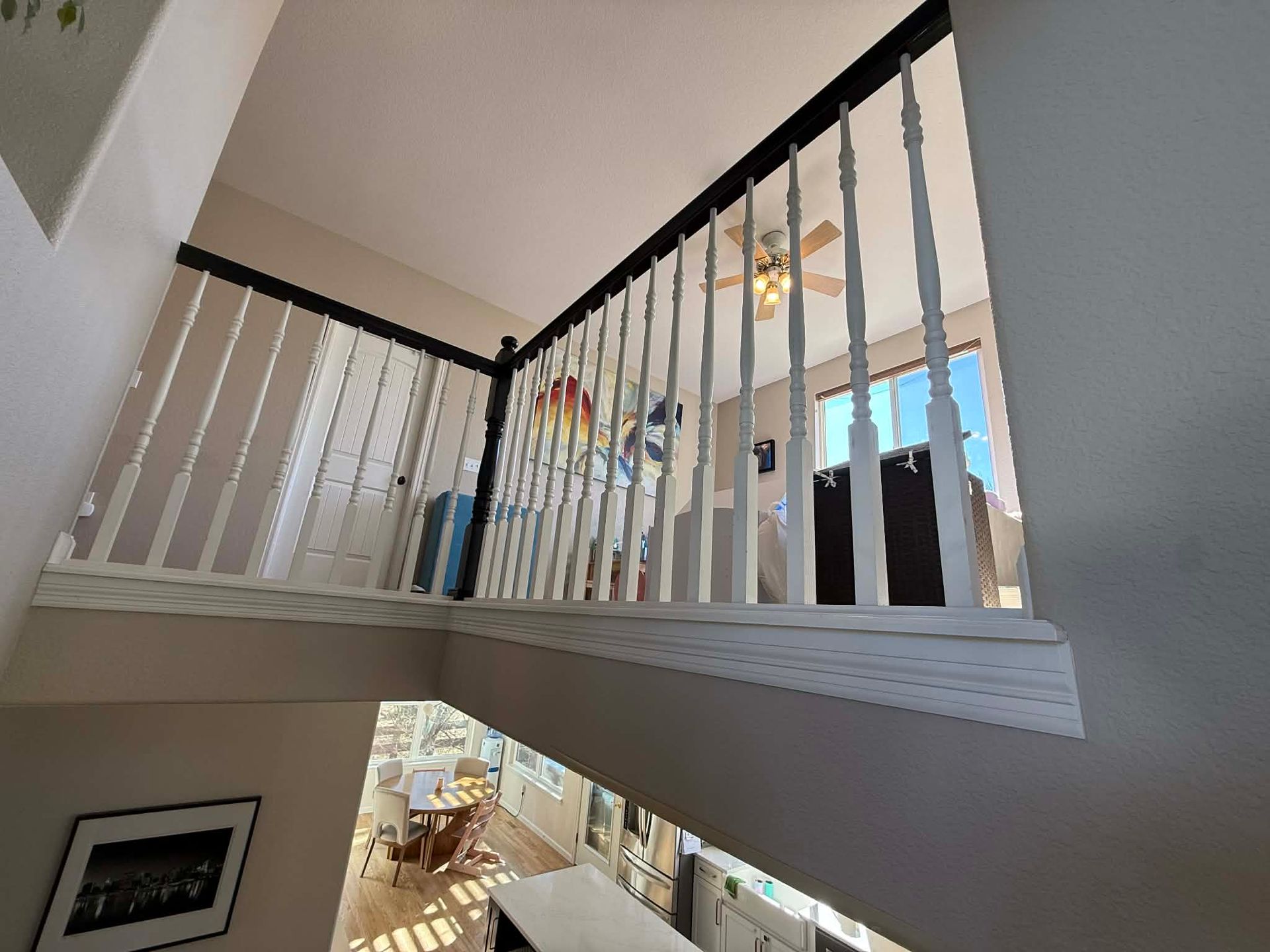 A view from an upper landing looking down at a lower floor, featuring white railings and a ceiling fan in the background.