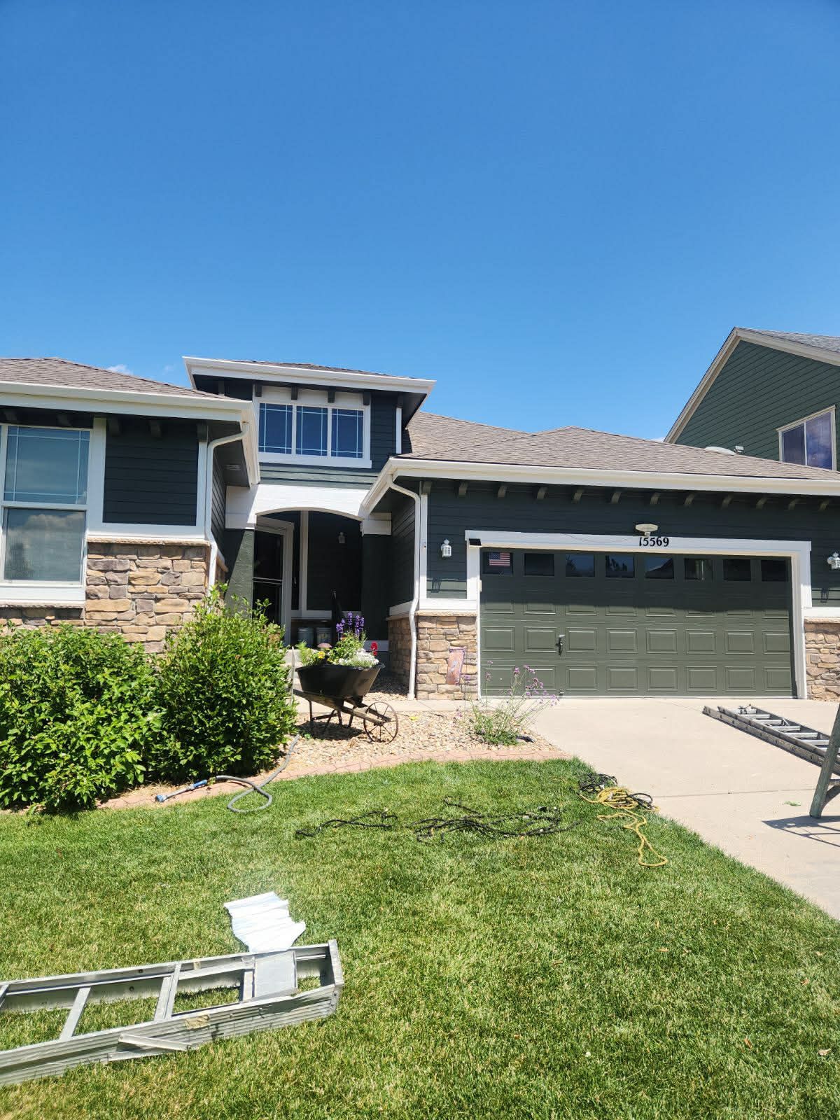 A two-story suburban home with dark grey siding, stone accents, a garage, and an entry path with a decorative cart.