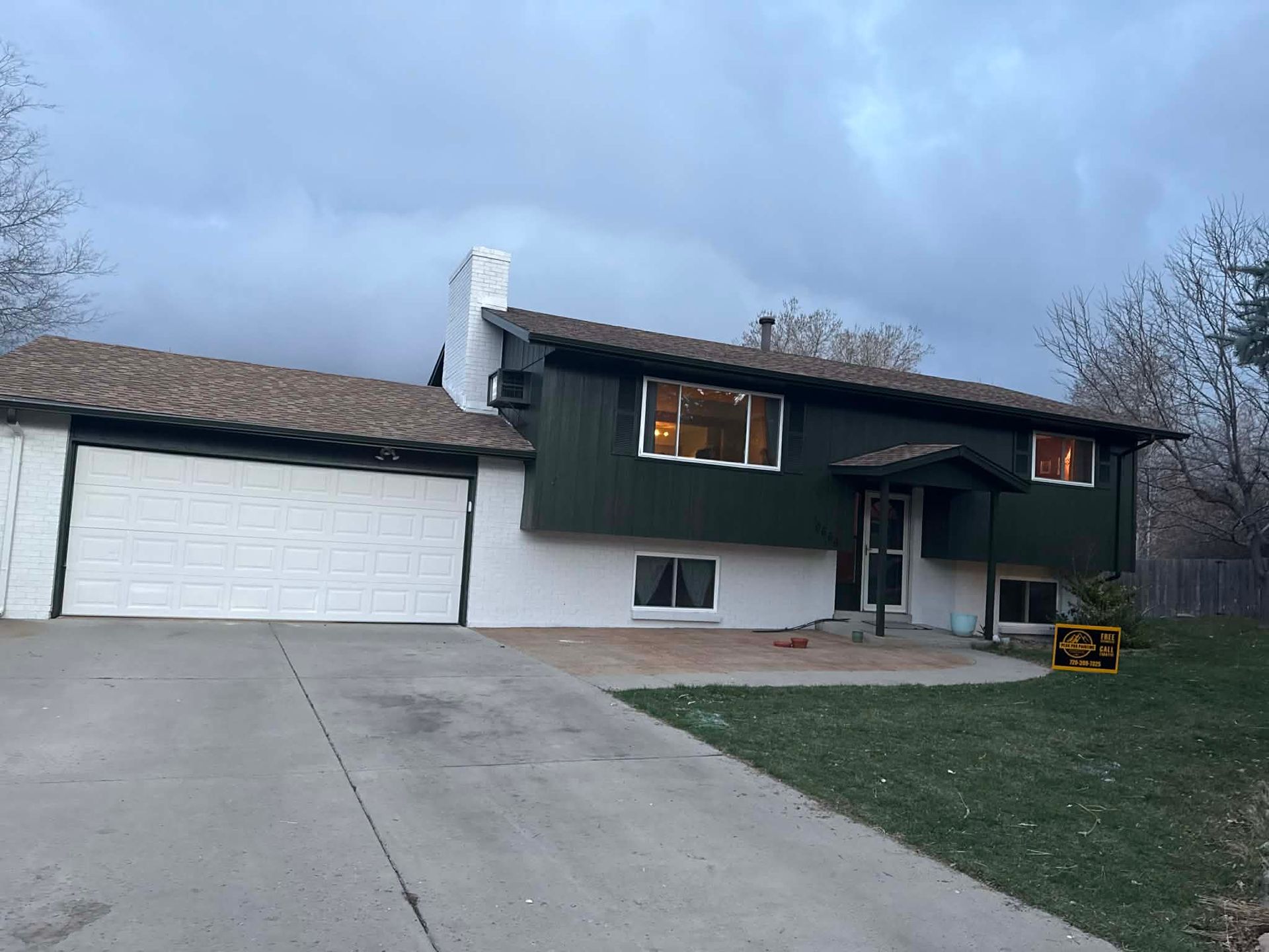 A split-level home with dark green siding, white stucco lower walls, a white garage door, and a concrete driveway.