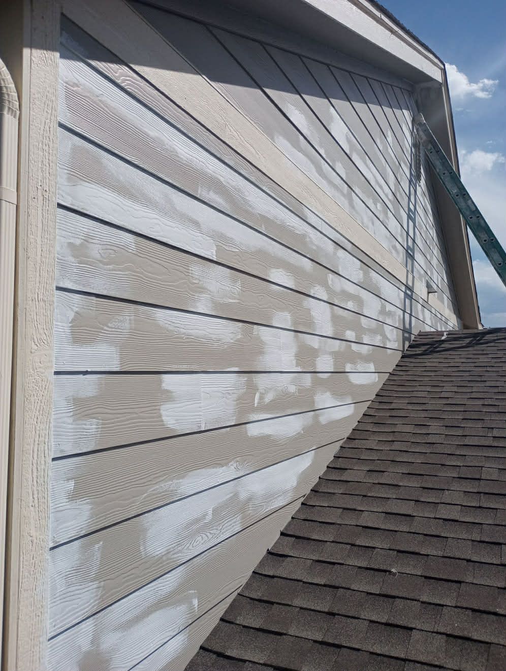 Exterior siding on a house being prepped for paint, showing areas of bare wood and remnants of old white paint.