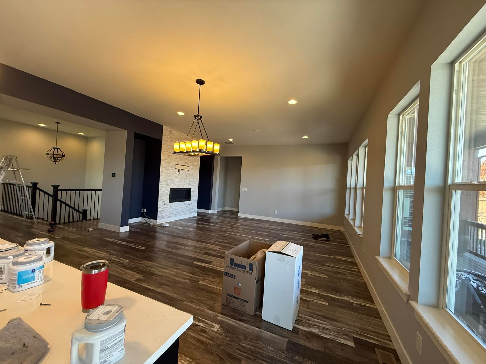 A spacious living area with dark wood floors, a brick fireplace, a chandelier, and cardboard boxes on the floor.