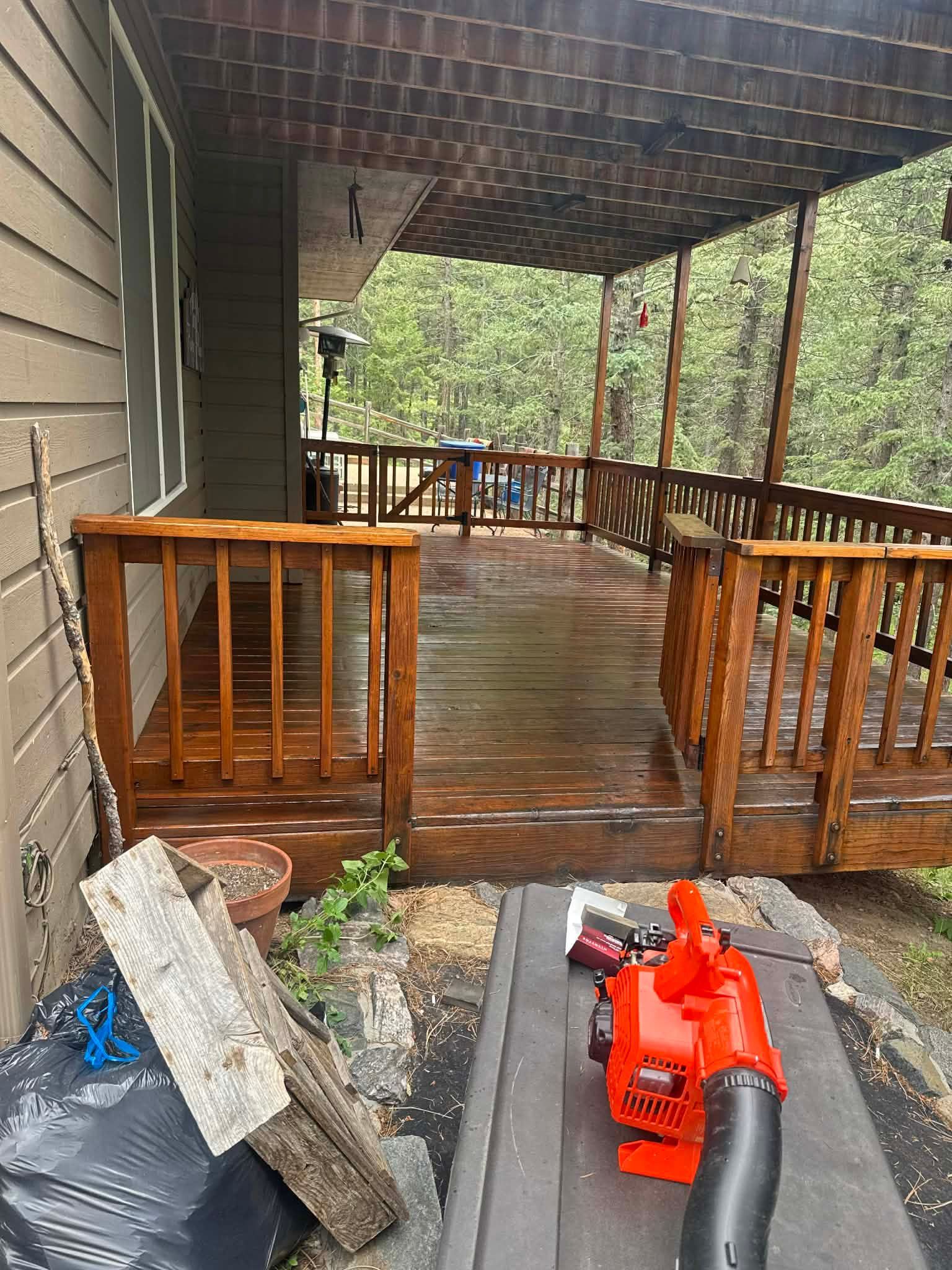 A wooden deck with railing under a pergola, with a bright orange leaf blower in the foreground.