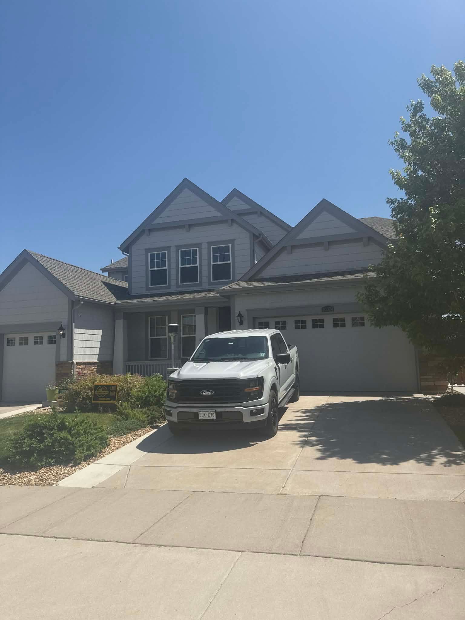 A white pickup truck parked in the driveway of a two-story gray suburban house under a clear blue sky.