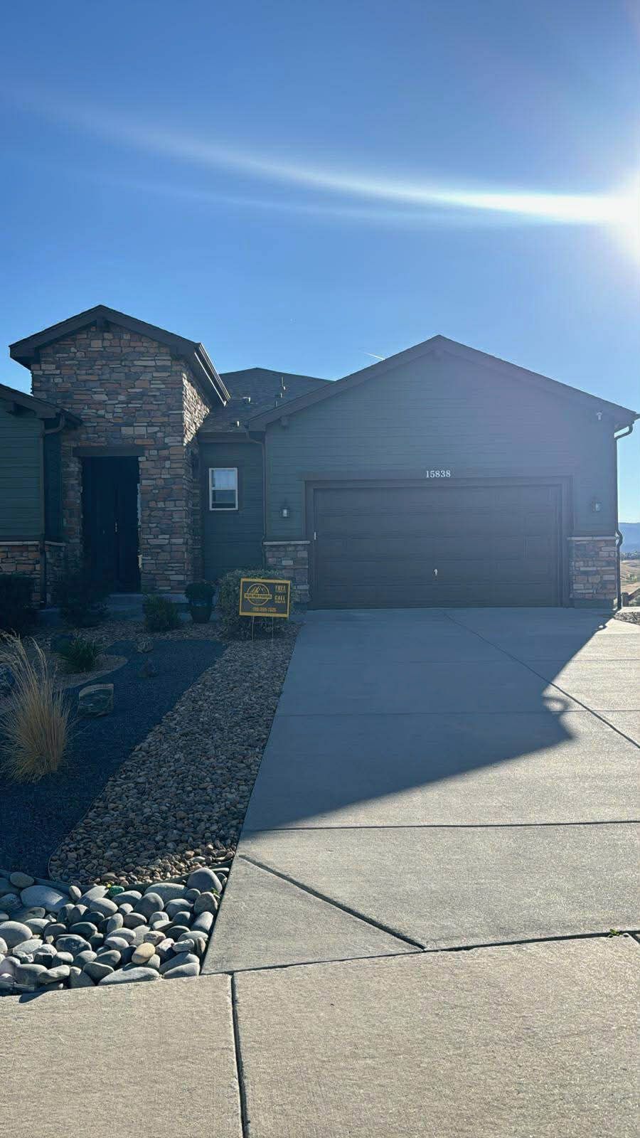 A single-story suburban house with dark siding, stone veneer accents, a double garage, and a concrete driveway.