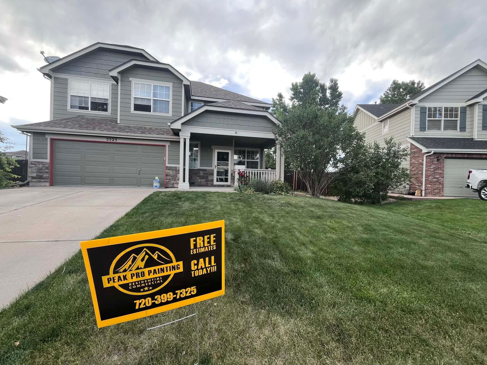 A residential house with gray siding and a front lawn featuring a yellow and black 