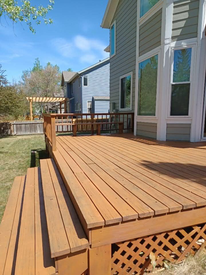 A brown wooden deck with stairs and lattice skirting, attached to a two-story house under a clear blue sky.