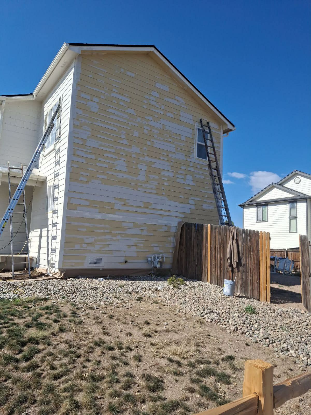 A two-story house with peeling yellow paint on the side, featuring two ladders propped against the exterior walls.