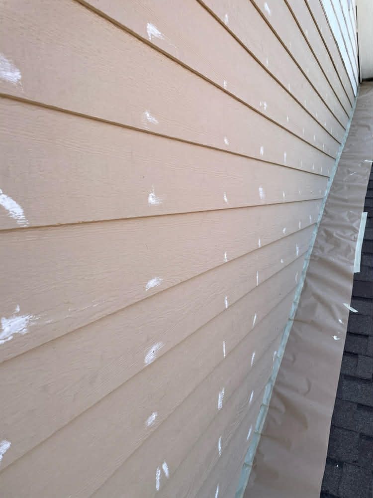 Side view of tan horizontal siding marked with white paint spots above a roof protected by brown construction paper.