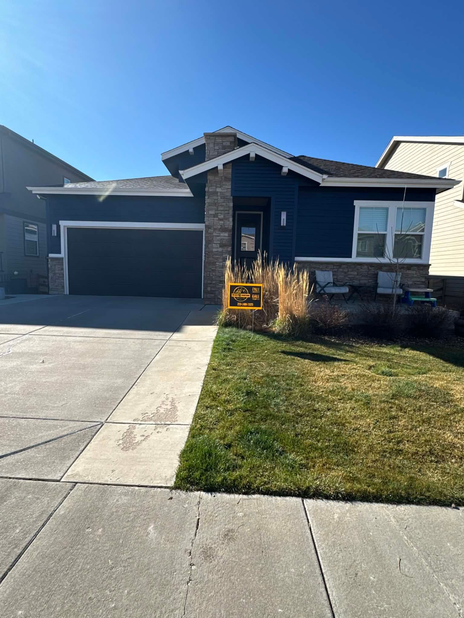 A dark blue single-story suburban house with a stone accent pillar, garage, and front lawn under a clear blue sky.