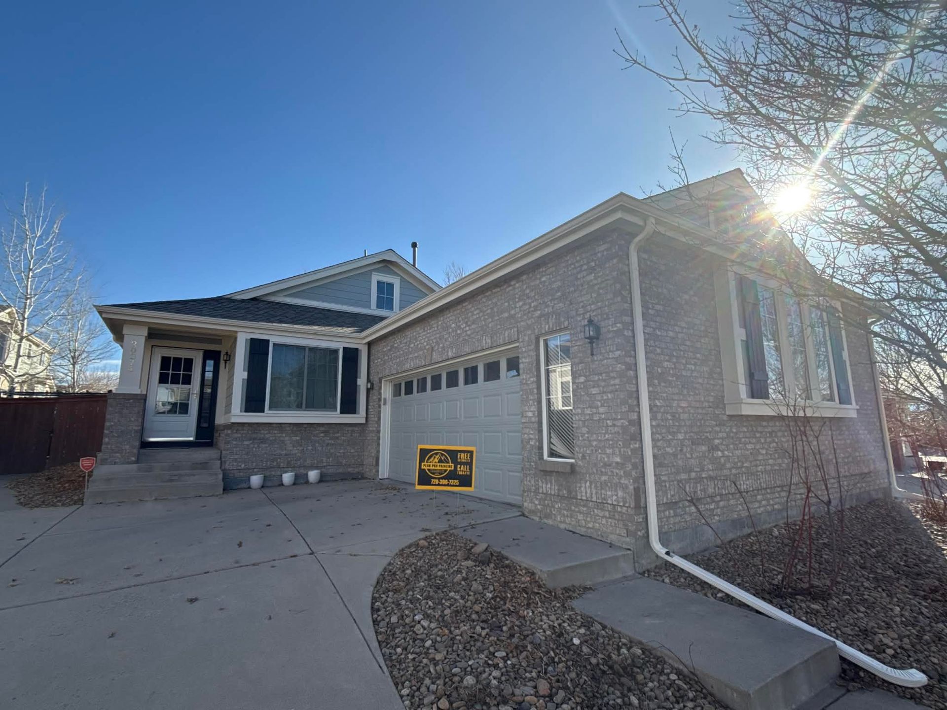 A suburban house with a gray brick exterior, a single-car garage, and a driveway, captured on a bright, sunny day.