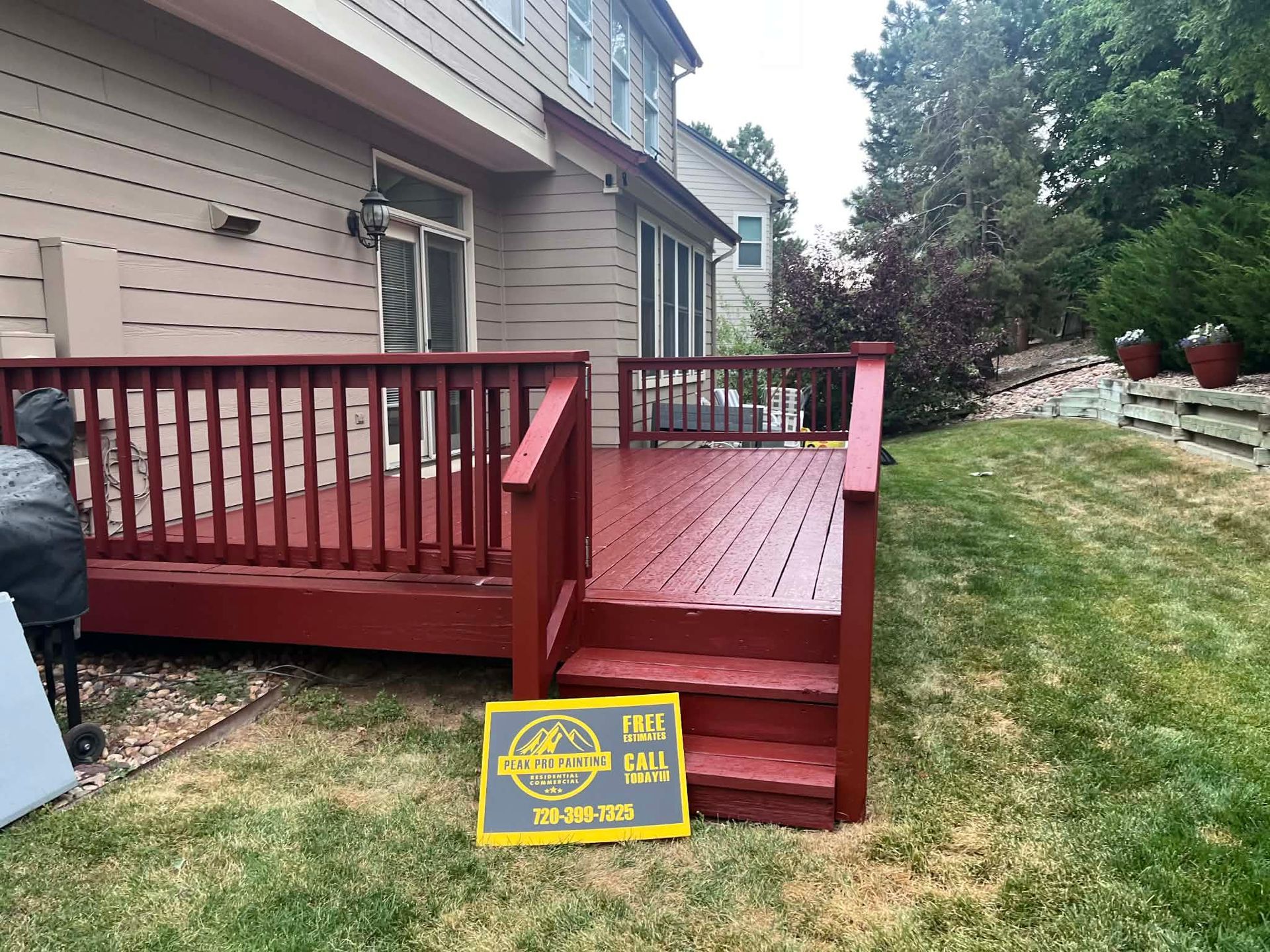 A freshly painted, deep red wooden deck with stairs and railings attached to the back of a tan house.