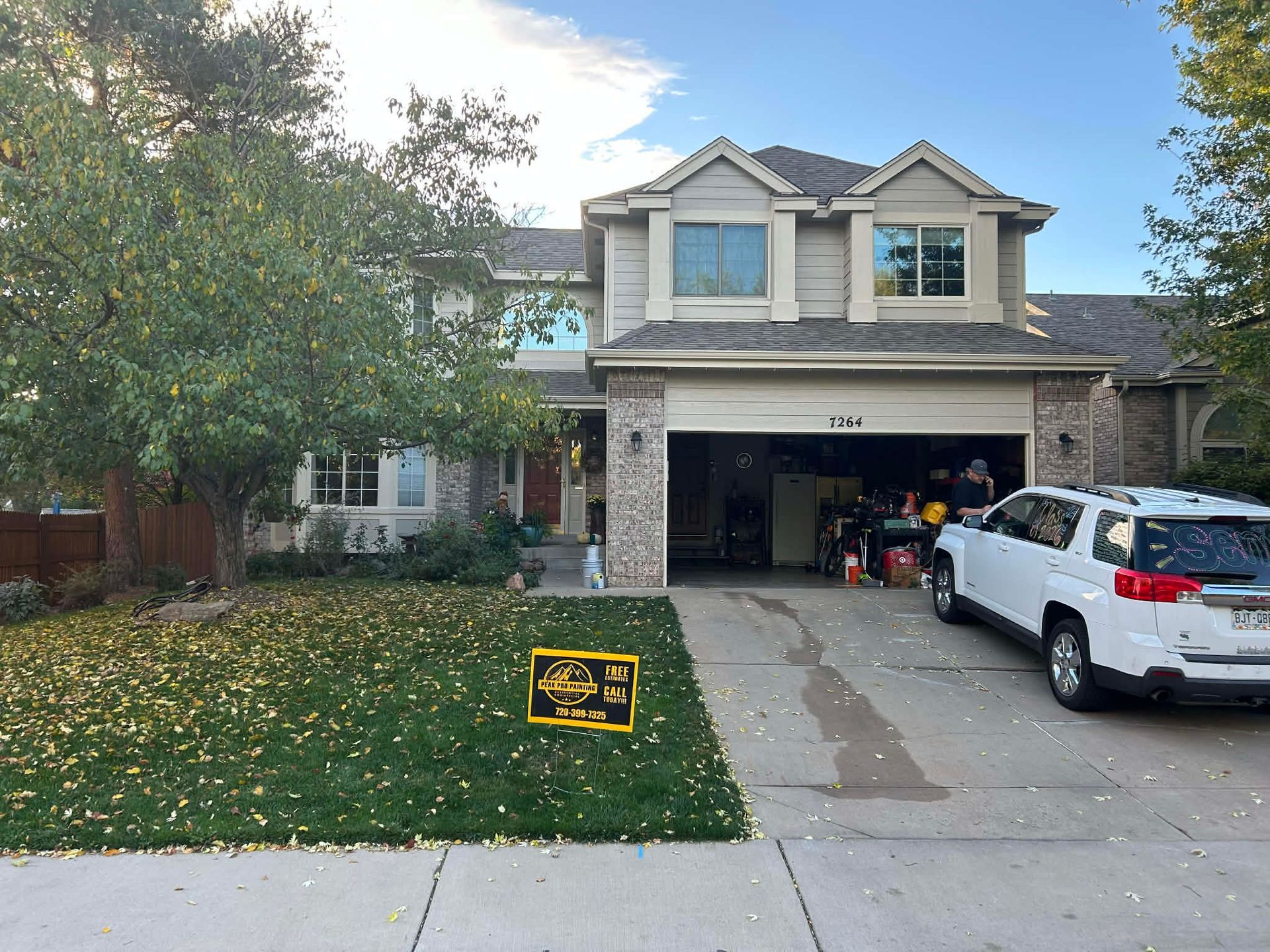 A two-story suburban house with a tan exterior, stone accents, and a white SUV parked in the open garage.
