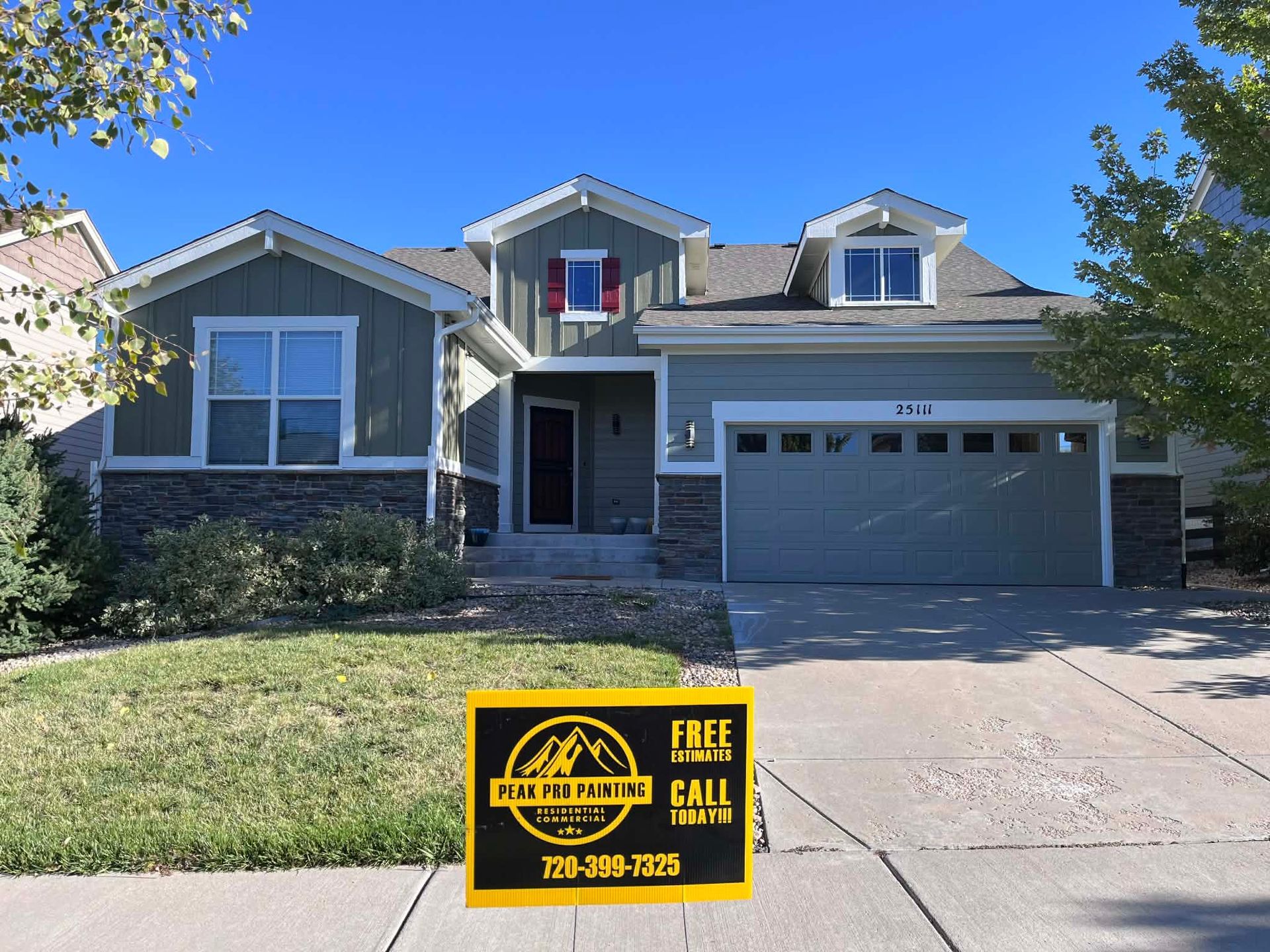 A green, single-story suburban house with a two-car garage and a yellow sign on the front lawn.