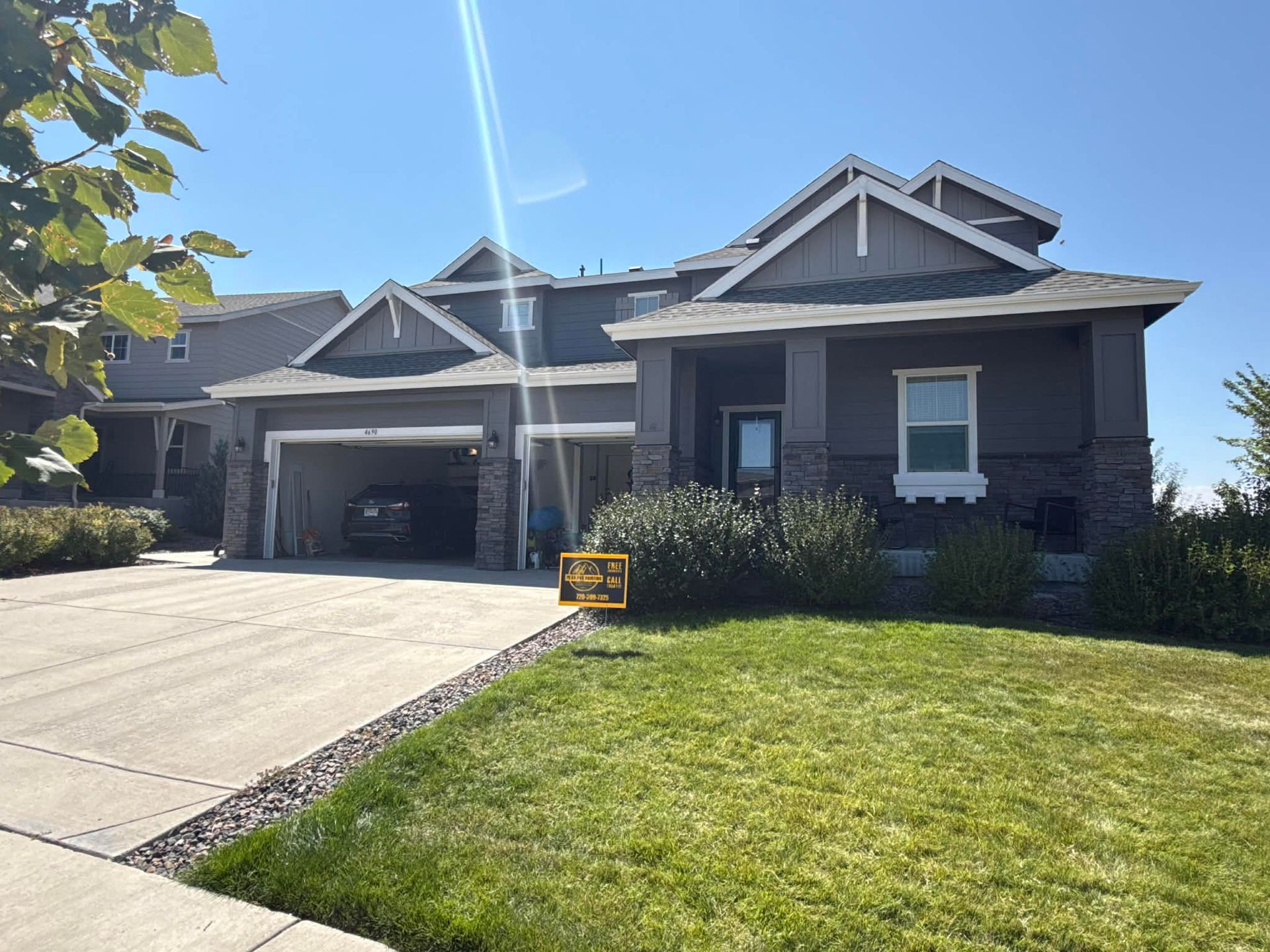 A single-story suburban house with a two-car garage, gray siding, stone accents, and a well-maintained green lawn.