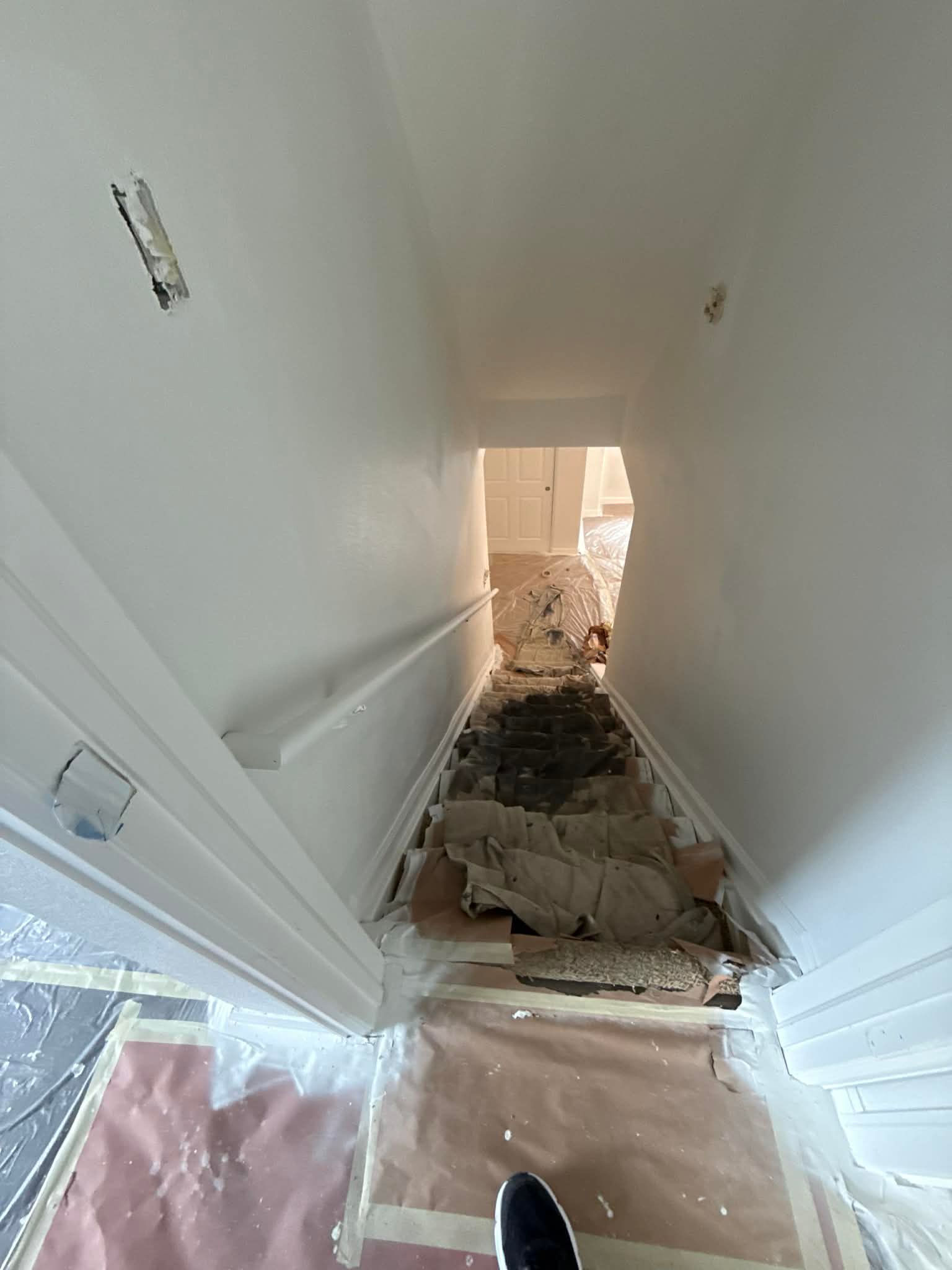 A hallway under renovation with brown paper covering the floor, white walls, and debris leading to a bright doorway.