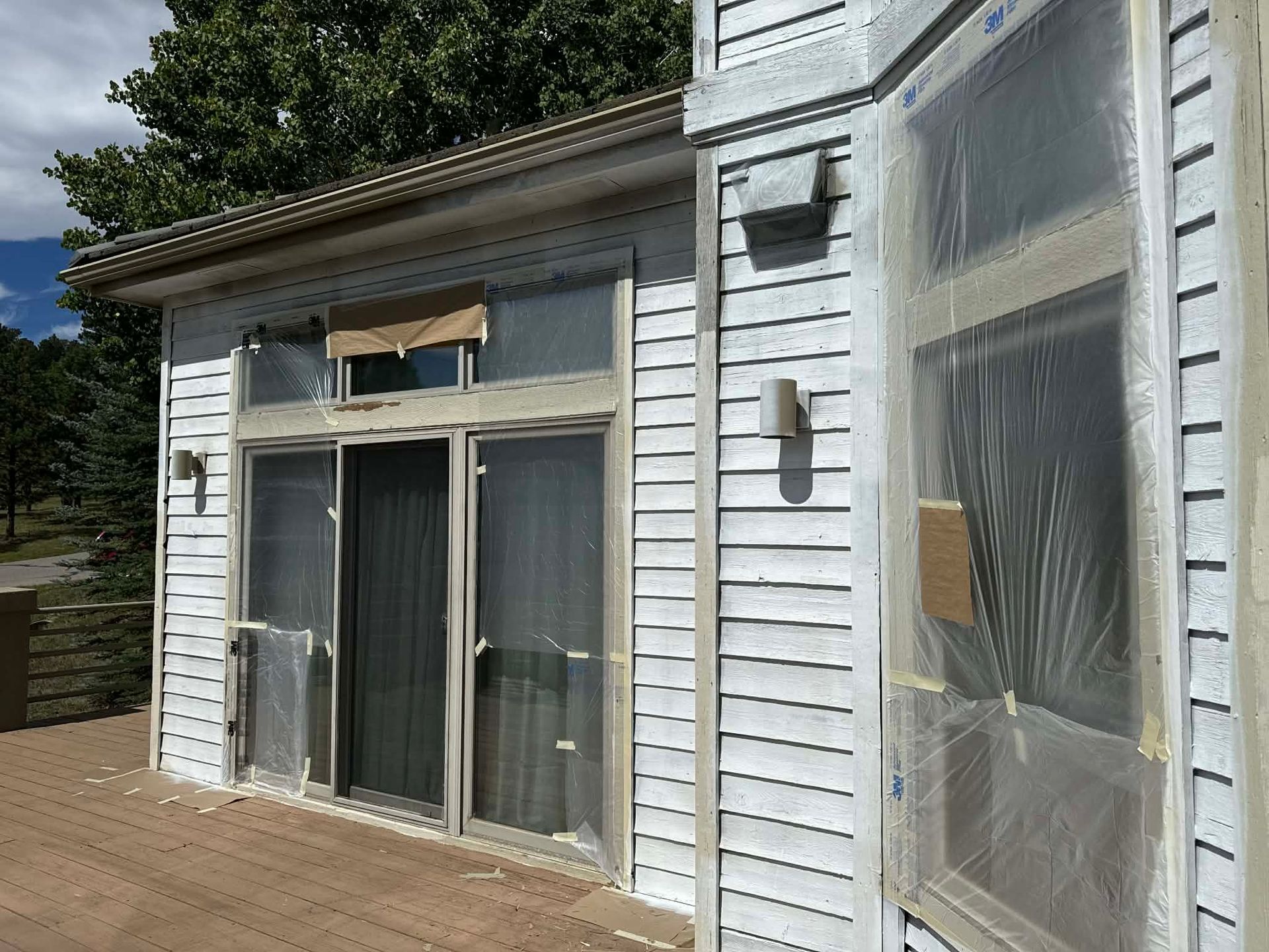 White house exterior with patio sliding glass doors covered in protective plastic film for painting or renovation.