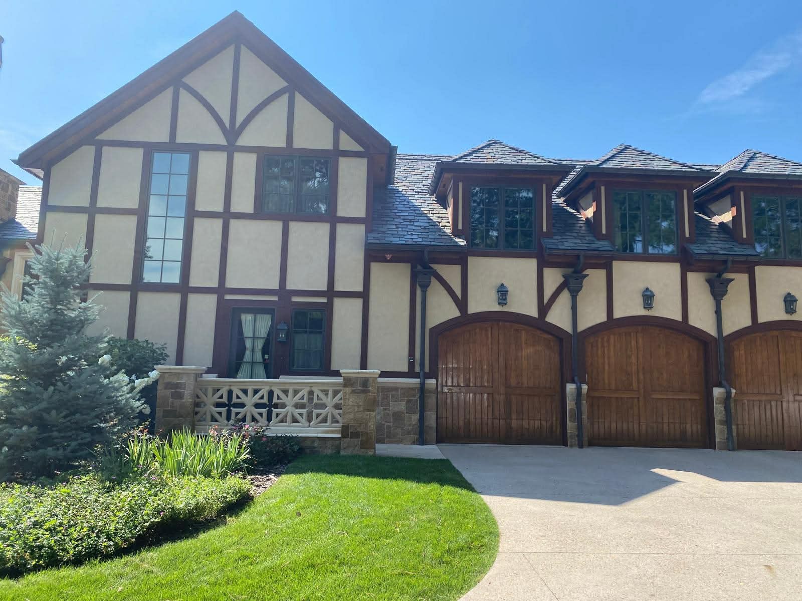 A two-story Tudor-style home with light stucco, brown timbering, three garage bays, and a well-manicured front lawn.