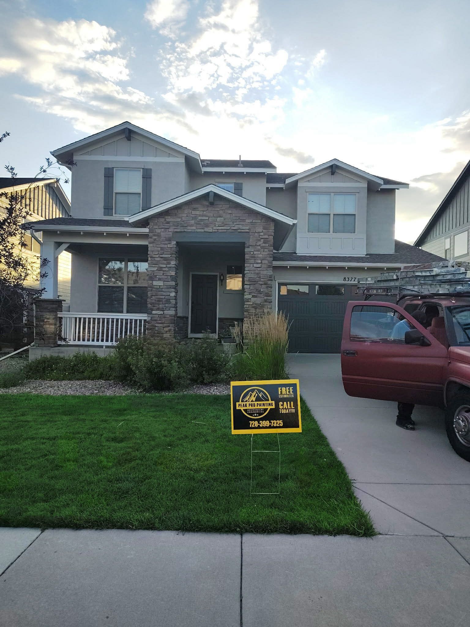 A tan two-story house with stone accents, a lawn, and a red truck parked in the driveway.