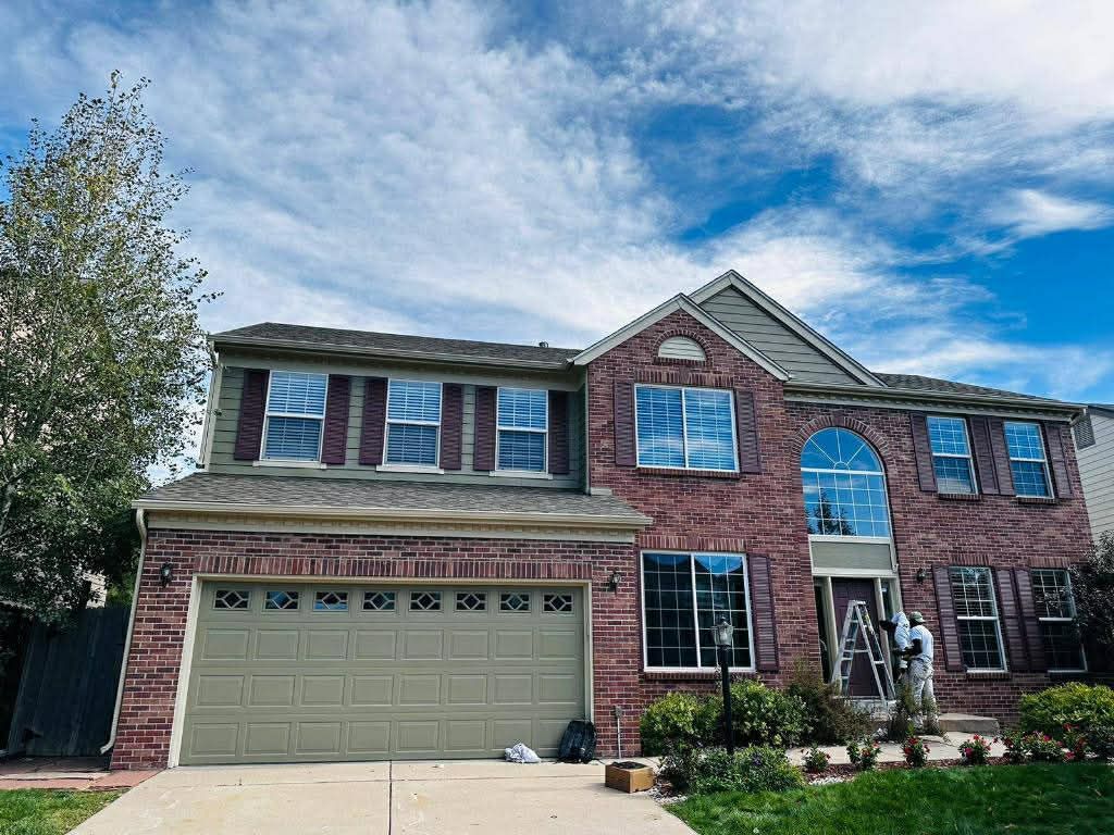 A multi-story brick suburban house with a two-car garage under a cloudy blue sky.