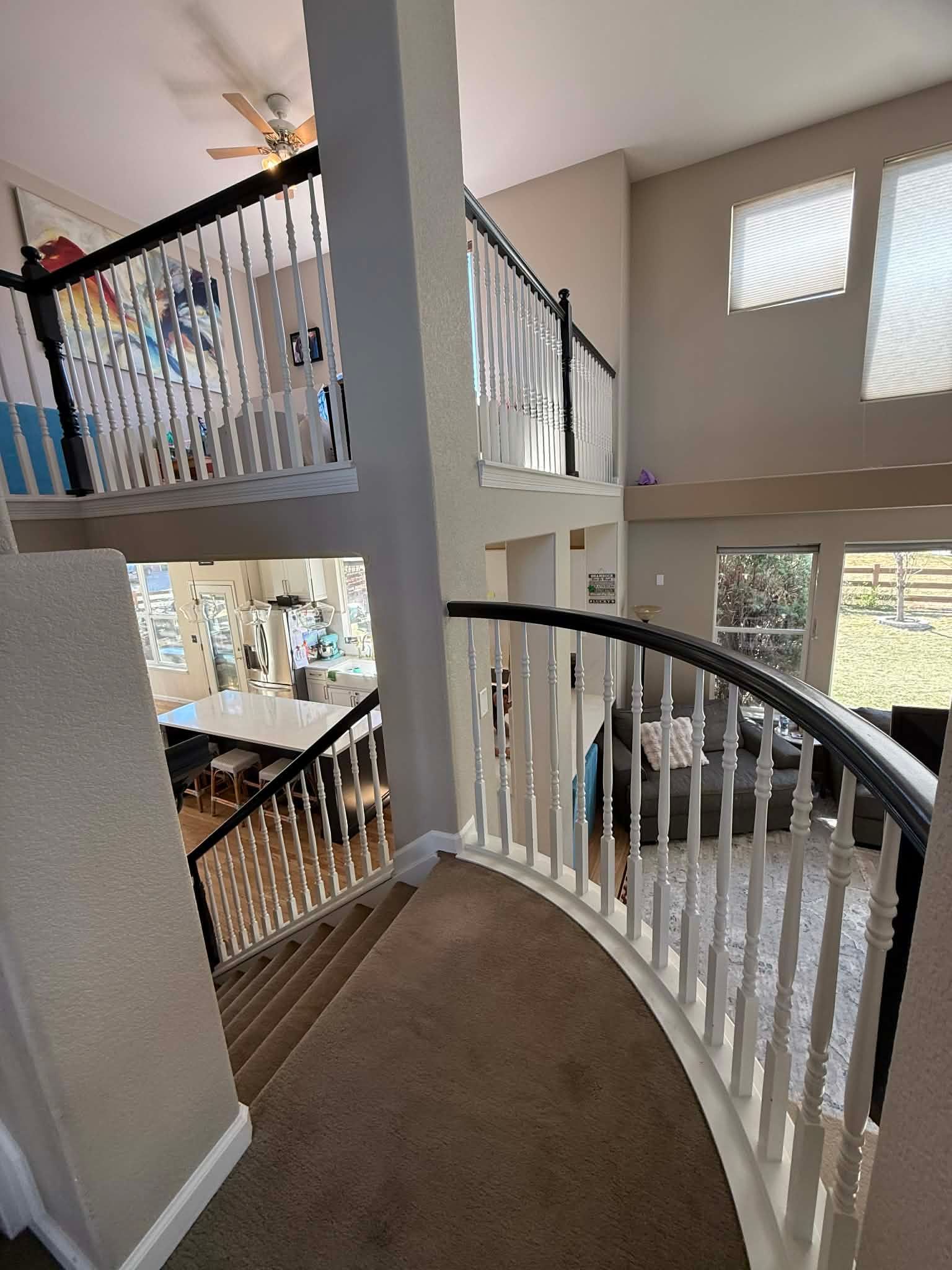 A view from a curved carpeted stair landing looking down into a two-story home with a kitchen and living area.