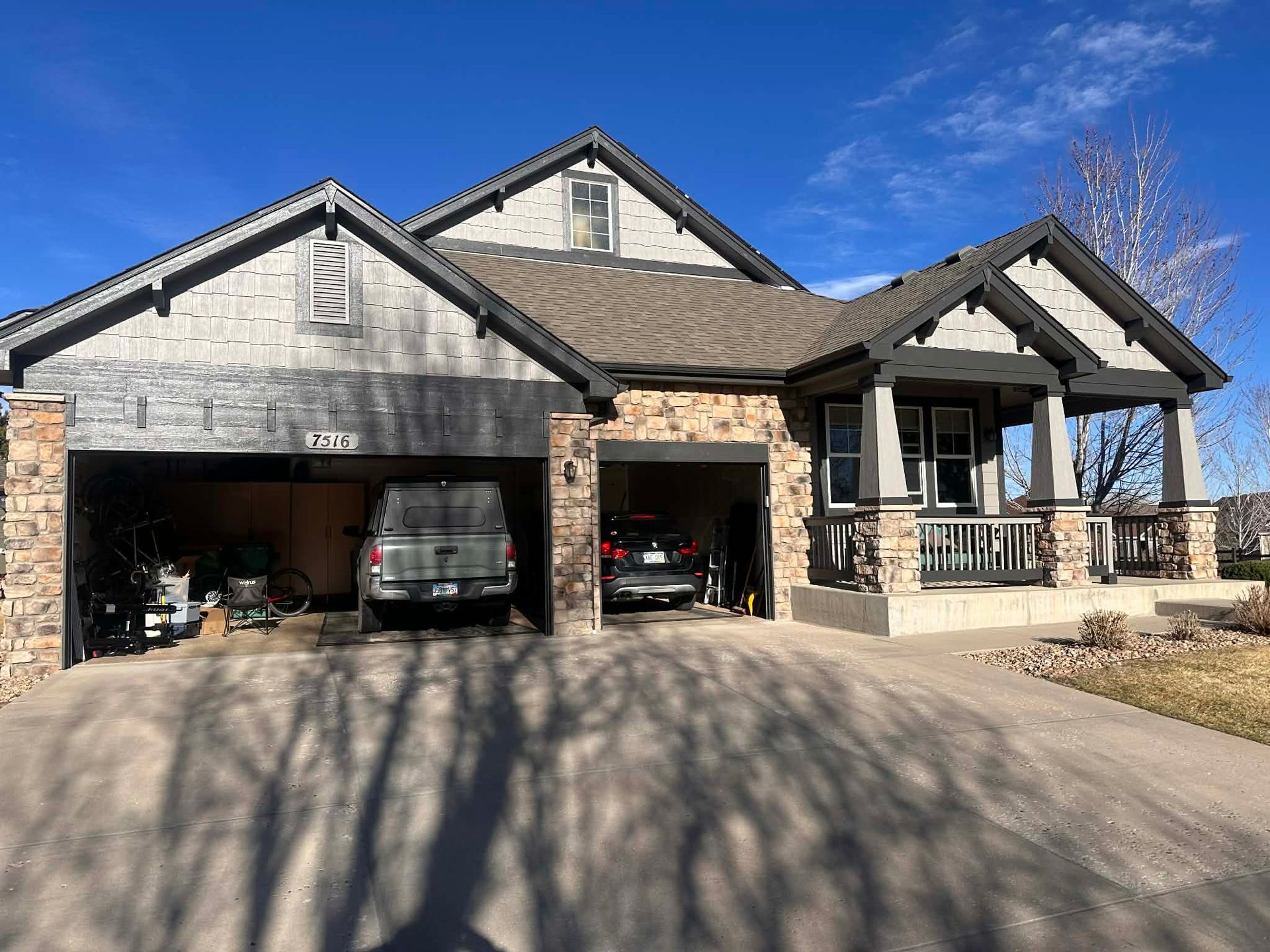 A multi-level home with a two-car garage, stone and siding exterior, and a front porch under a clear blue sky.