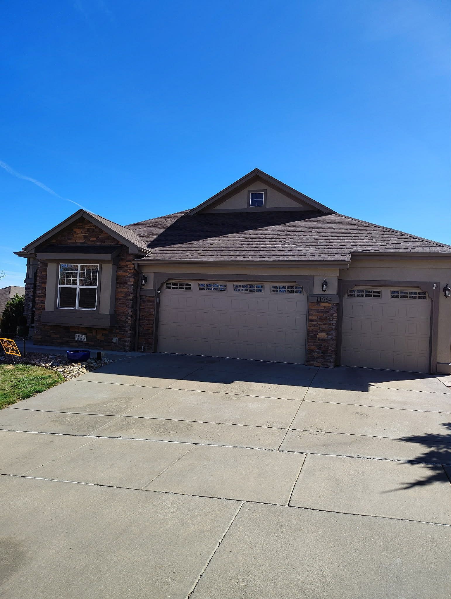 A suburban single-story house with a three-car garage, stone accents, and a concrete driveway under a clear blue sky.