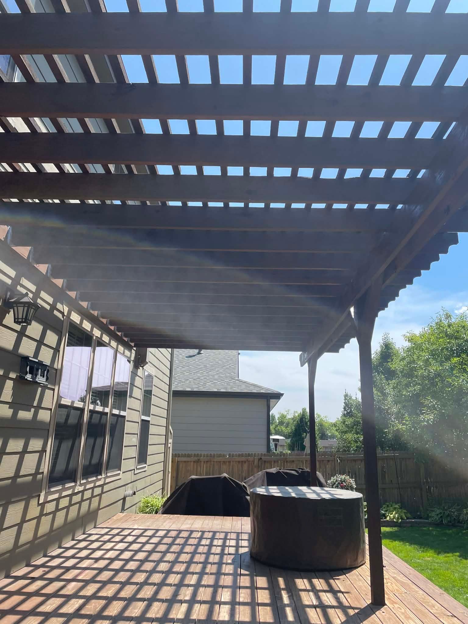 A wooden pergola casts striped shadows onto a backyard deck with a covered item in the foreground.