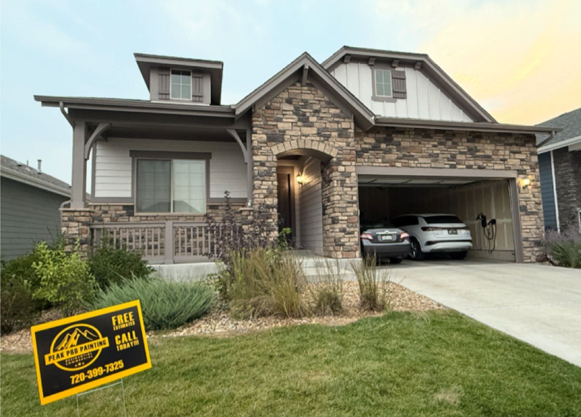 A suburban house with stone veneer, a front porch, and an attached two-car garage, with a real estate sign in the yard.