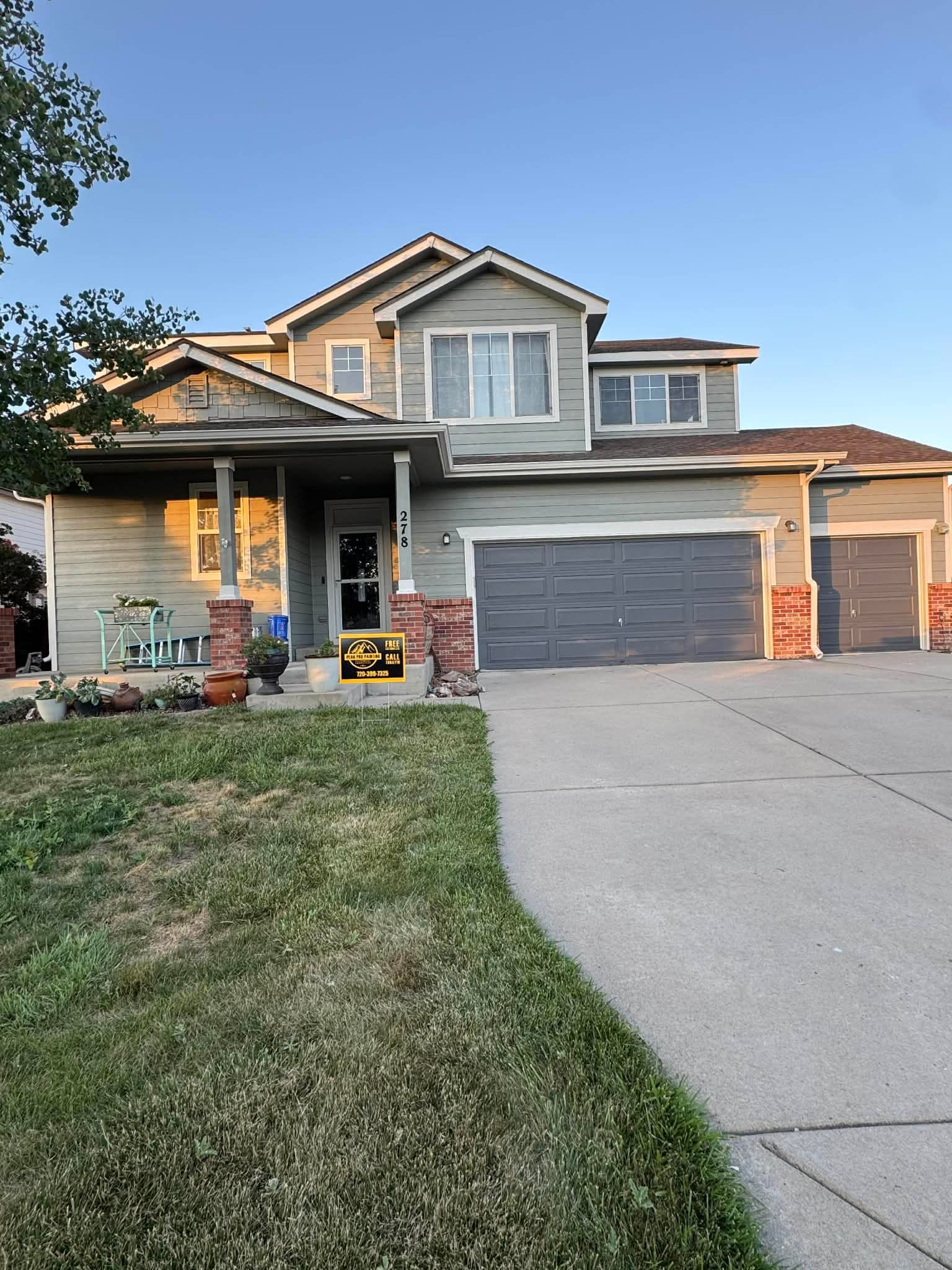 A two-story gray house with a multi-car garage, brick accents, and a front porch, under a clear blue sky.