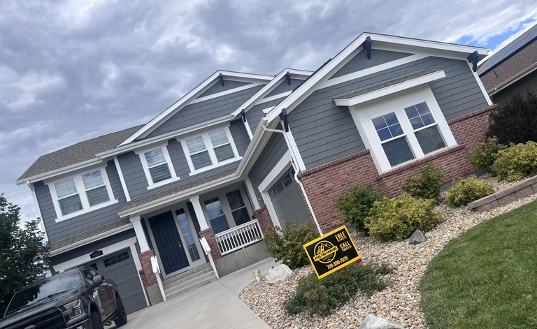 A two-story house with dark gray siding and brick accents, featuring a front-facing garage and a landscaped front yard.