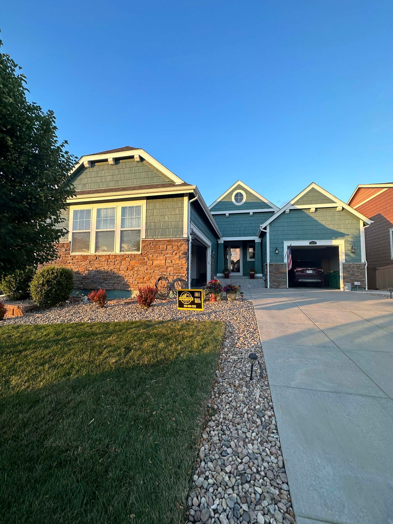 A single-story suburban house with sage-green siding, brick accents, a gray shingle roof, and an attached two-car garage.