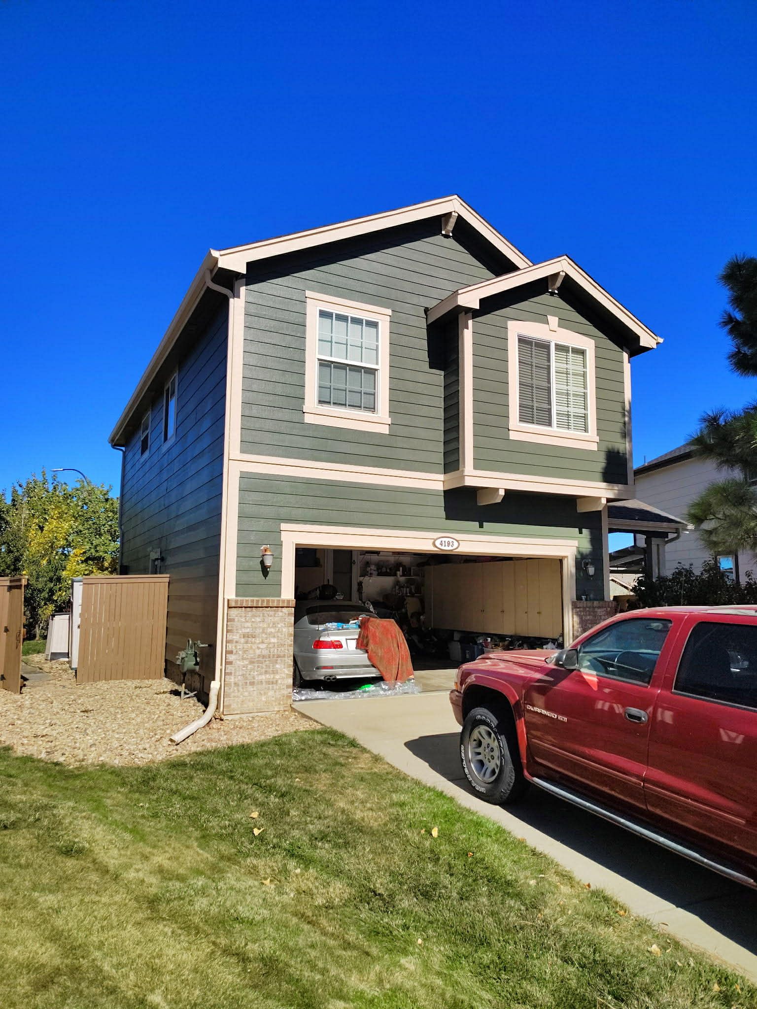 A dark green, two-story house with a garage, light-colored trim, and a red truck parked in the driveway.
